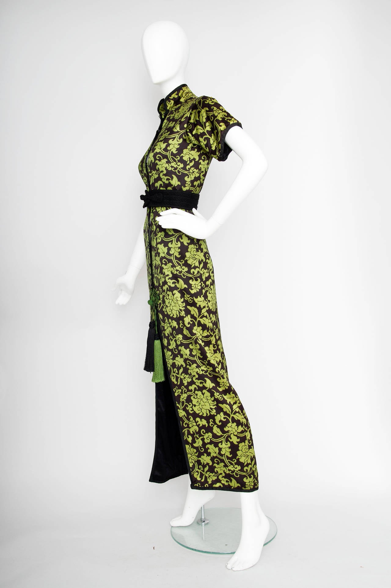 A stunning 1970s asian style Yves Saint Laurent floor length evening dress with an all over bright green floral print, short sleaves a high mandarin collar and black satin trimming. The dress furthermore features a green and black tassel detail that