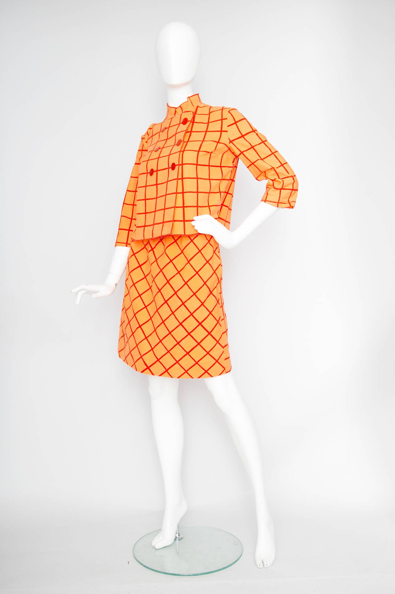 A lovely 1960s Marimekko two piece cotton color block ensemble in orange with bold red stripes. The ensemble features a cropped boxy jacket and an a-ilne miniskirt. 

The double breasted jacket features a front wrap closure with six red buttons, a