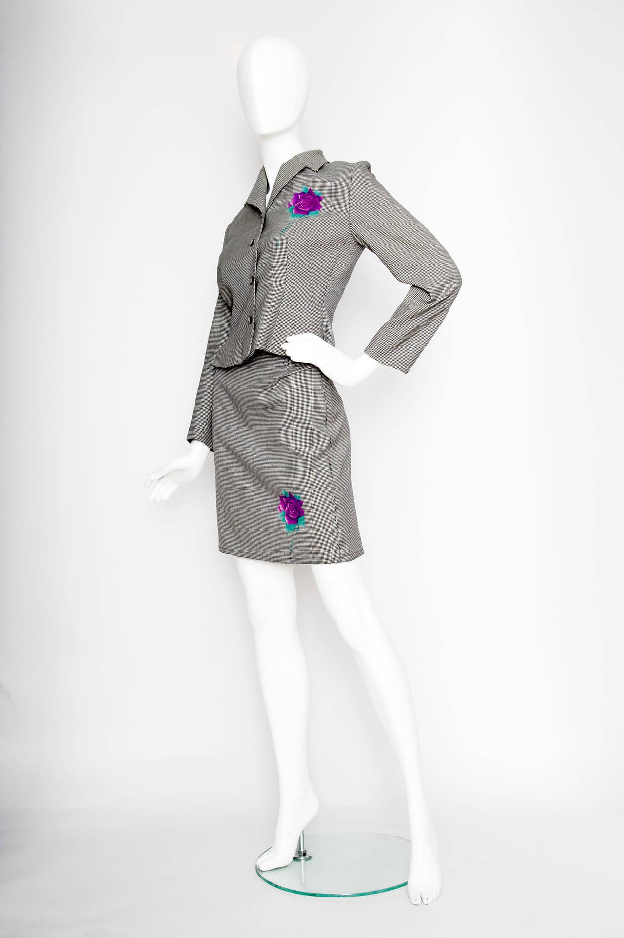 A gorgeous 1980s monochrome Gianni Versace wool skirt suit with multiple bright purple and green rose prints. The roses are placed symmetrically on both jacket and skirt and add to the graphic nature of the suit. The jacket has a full front button
