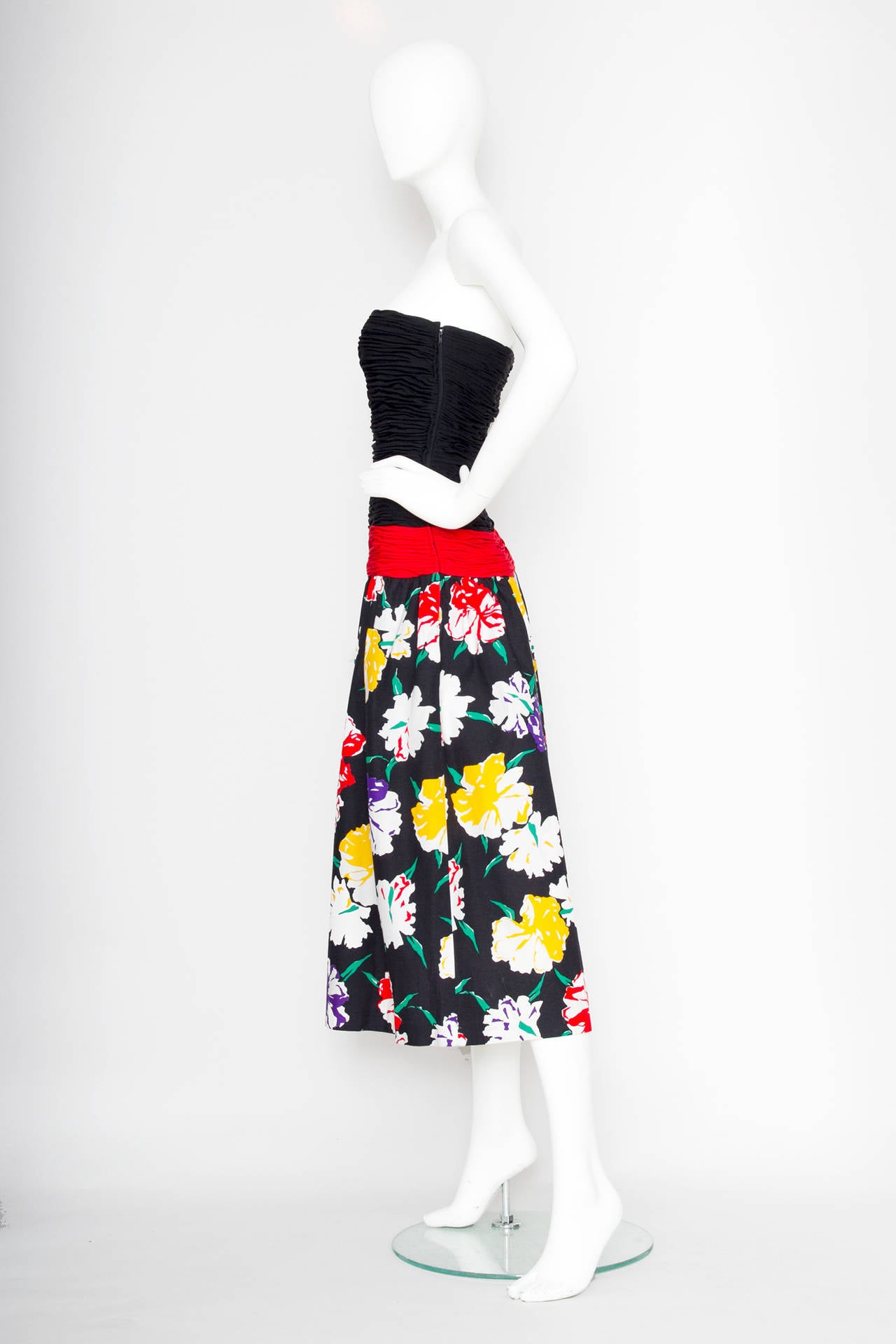 A 1980s Valentino cotton dress with a full floral printed skirt and a fitted ruched bodice, two side pockets and a red sash stretches gently across the hips. The dress closes in the side with a simple zipper and a hook & eye closure.

The
