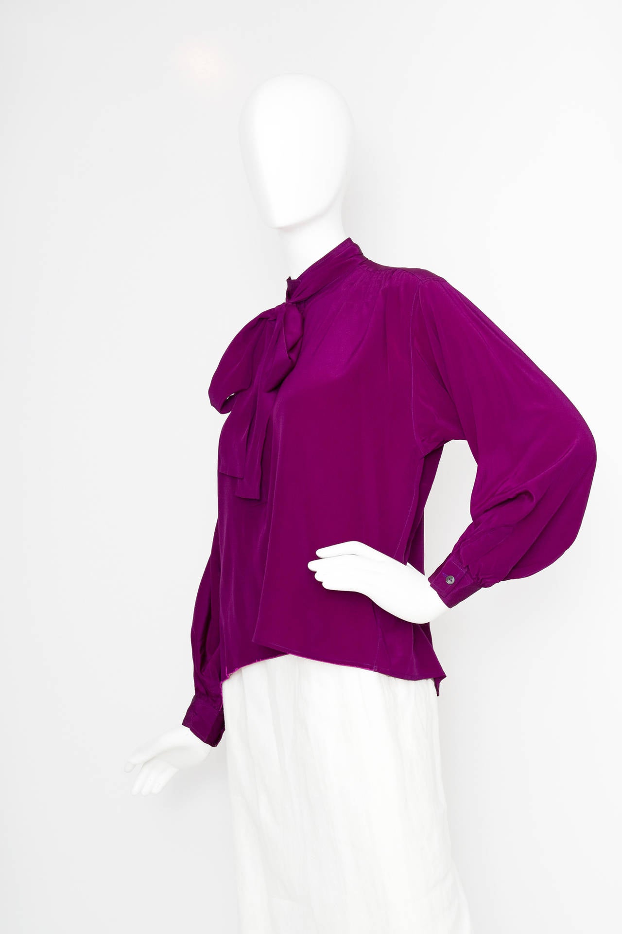 A 1980s Yves Saint Laurent plum coloured silk blouse with a button down front, one buttoned cuffs and a pussy bow detail.

The skirt is equivalent to a modern size Medium.