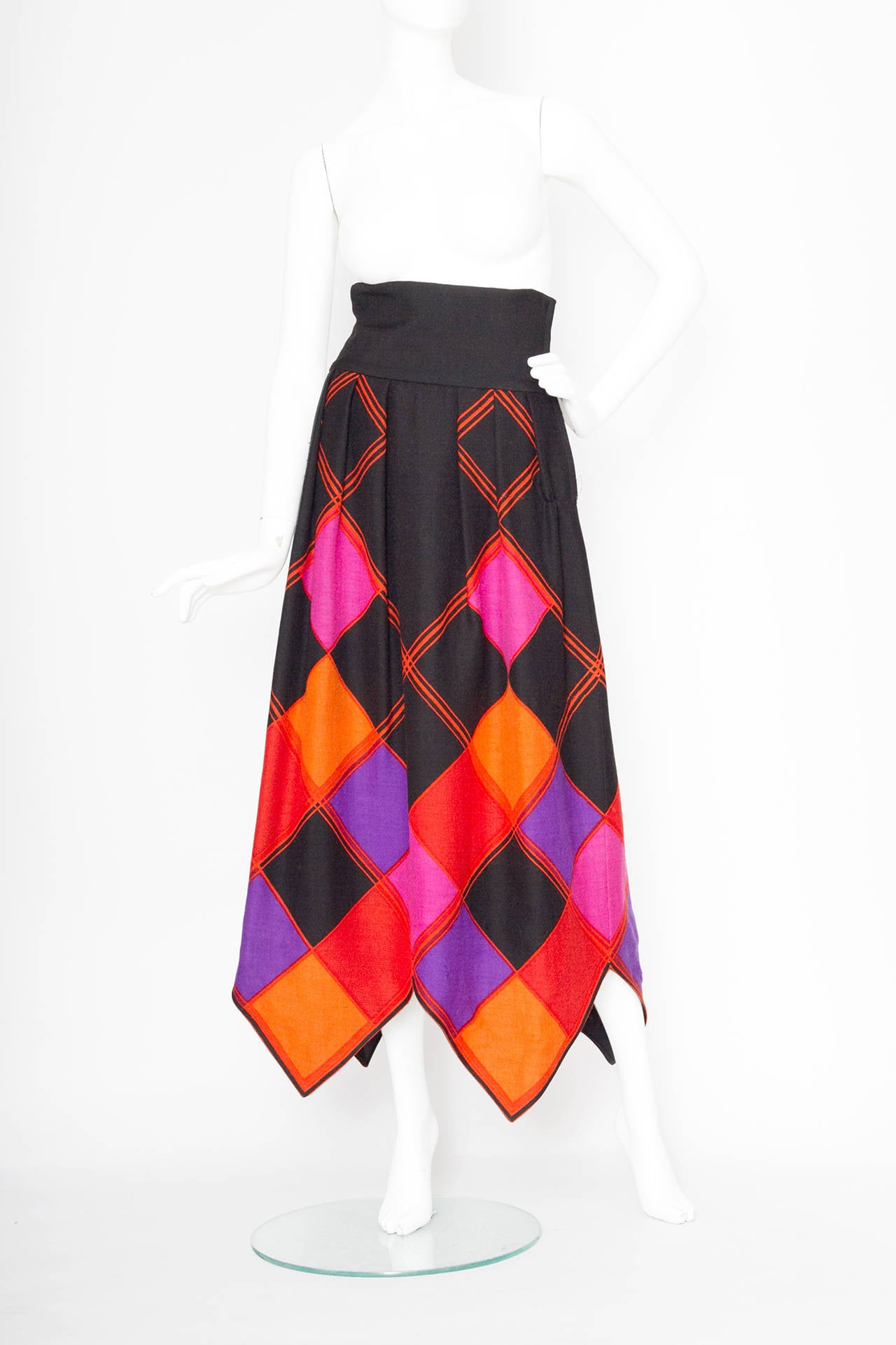 An amazing 1970s black Pierre Cardin op art inspired wool skirt with a graphic print in orange, red, purple & pink. The a-line skirt has a wide sash around the waist and an uneven hemline gently mirroring the illusionist print. The skirt closes in