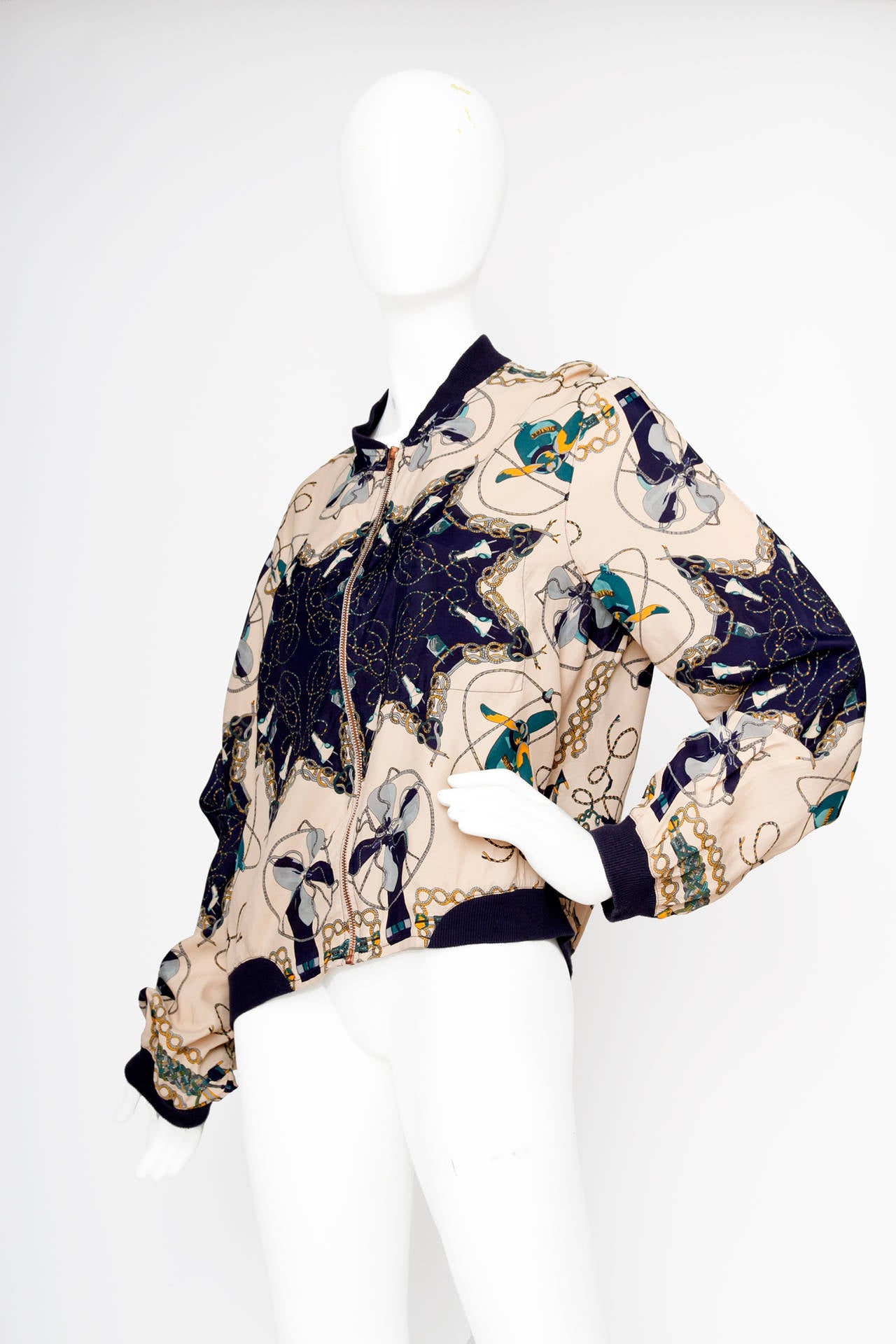 An amazing 1990s Jean Paul Gaultier silk bomber jacket with an electrical appliance themed print. The jacket is held in a beige and navy colourscheme with green and yellow accent colours. The bomber closes in the front with a metal zipper closure