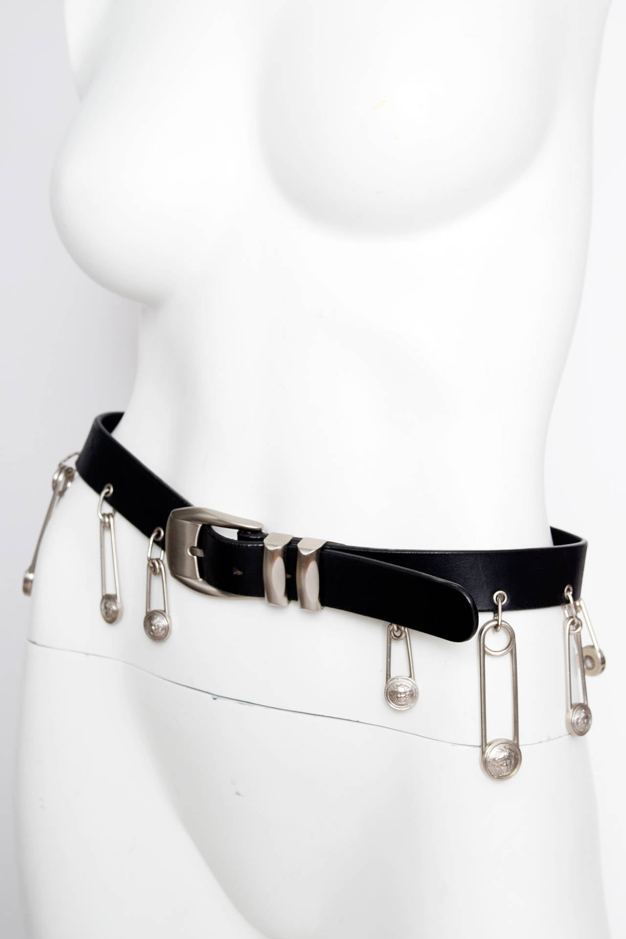 An iconic 1990s Gianni Versace black leather belt with silver hardware and exaggerated safety pin details.  The safety pins have the iconic medusa imprint and are in varying size. 

The belt holes are between 72 and 78.