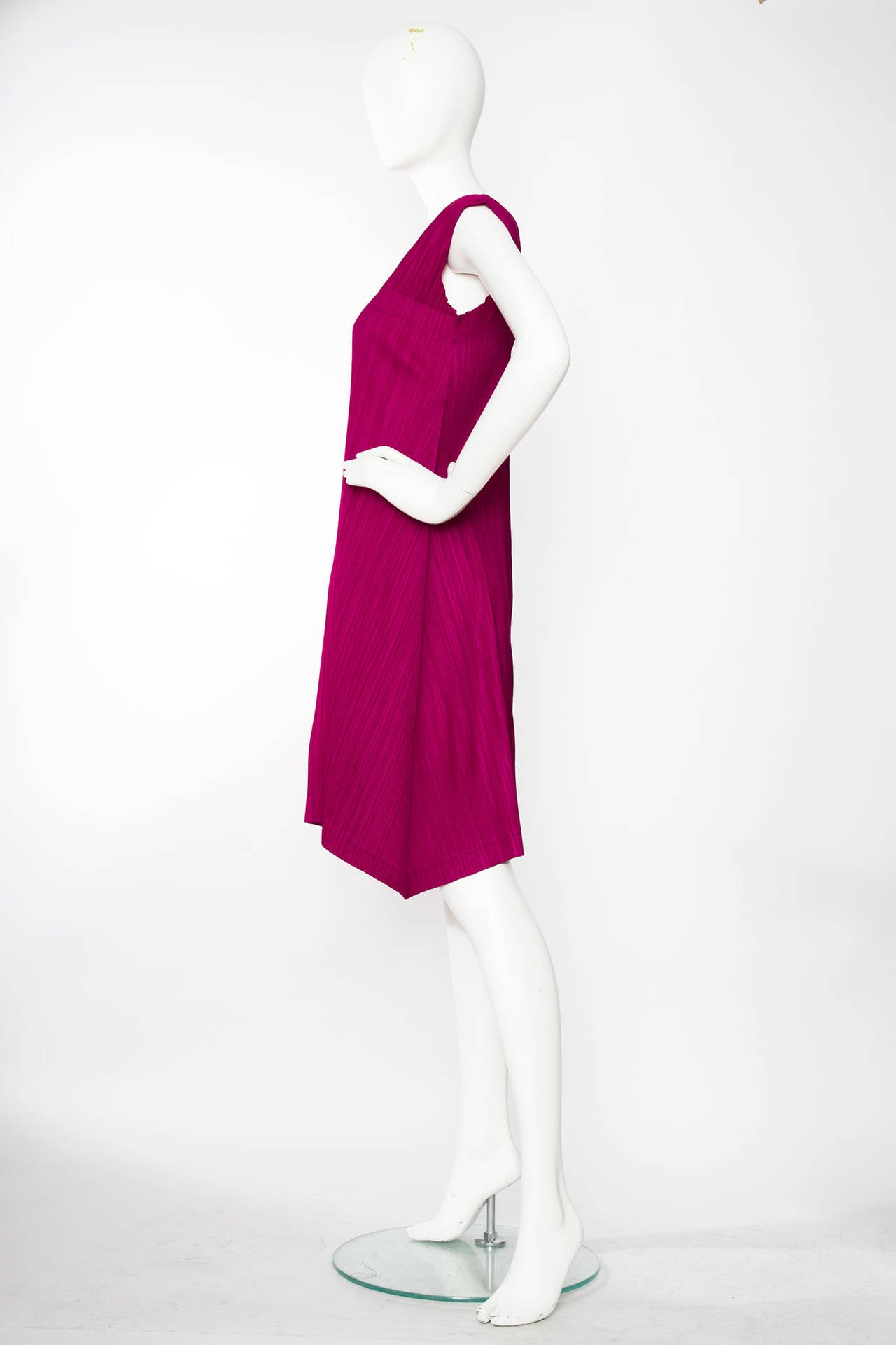 A stunning  fuchsia pink Pleats Please by Issey Miyake dress.with short cap sleeves and an asymmetrical front. The hemline cuts just above the knee and is made of 100% polyester. 

The size of the dress corresponds to that of a modern size