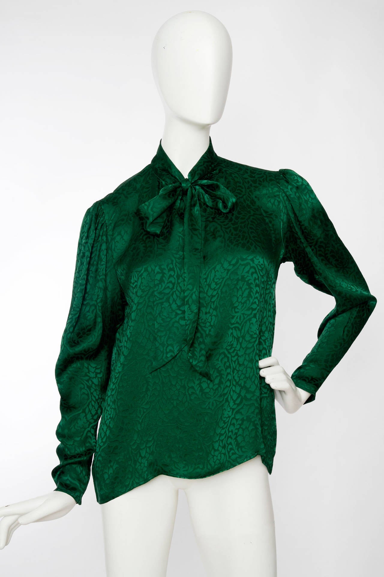 A lovely 1980s Yves Saint Laurent emerald green silk blouse with an allover paisley jacquard weave and bow detail around the neckline. The blouse has long tapered sleeves with a slight puffed shoulder and three buttoned cuffs. The blouse has a