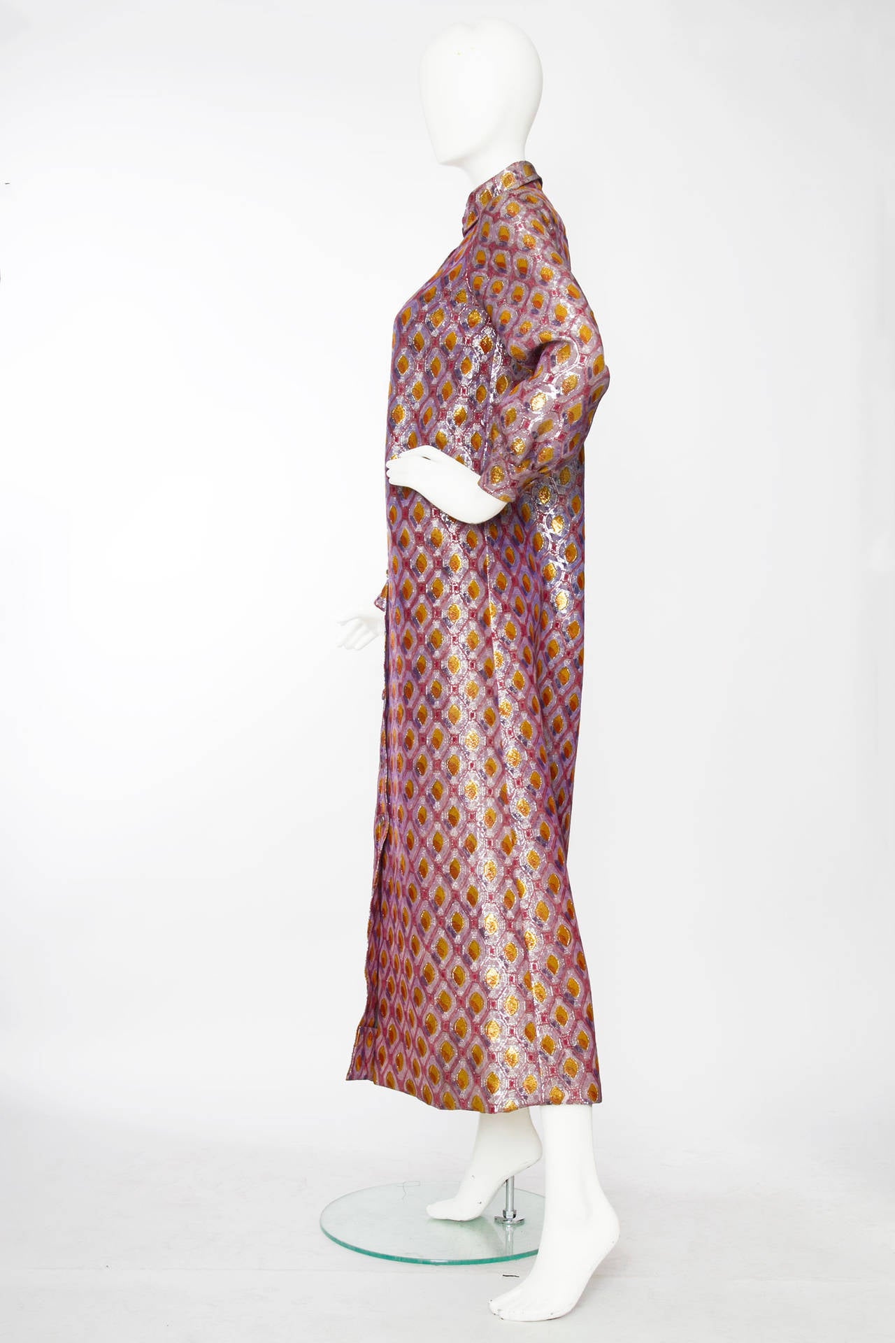 A 1970s Givenchy gold and silver lurex thread floor length coat with long sleeves and a full front button closure. The coat is in a grephic silk and lurex fabric in purple hues and yellow. The coat is fully lined and has a contrasting blue top