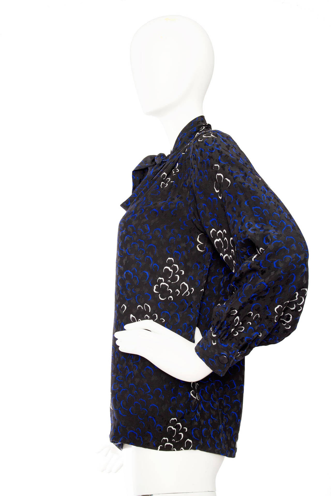 A lovely 1970s Yves Saint Laurent jacquard woven silk blouse with an allover abstract flower print in white and blue. The blouse has a tie collar and one buttoned cuffs and a button down front. 

The size of the blouse corresponds to that of a