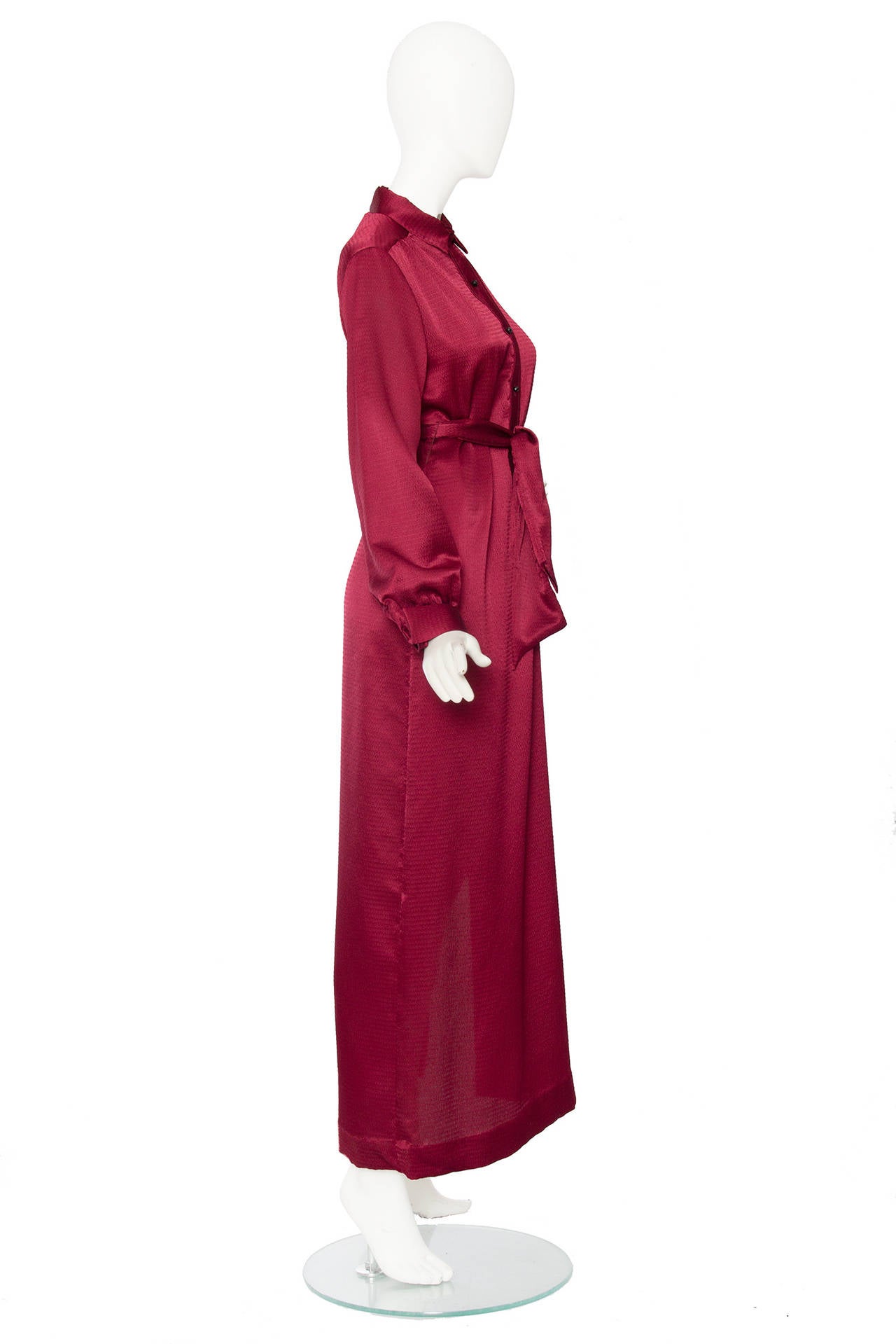 A 1970s Lanvin burgundy silk dress with long sleeves, a button down front with contrasting black buttons and a matching belt to tie around the waist. The long fitted skirt has a 50s long slit and one buttoned cuffs. 

The size of the dress