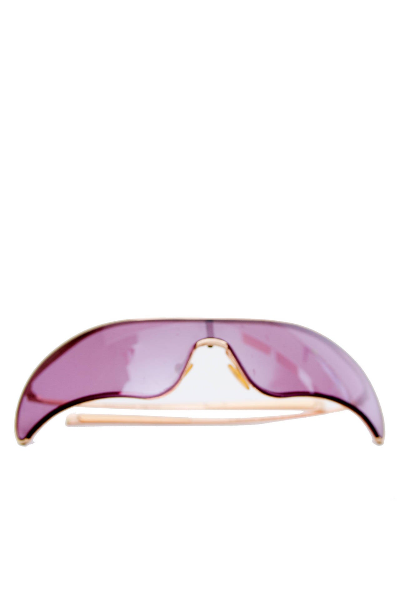 A pair of early 2000s Alexander McQueen sunglasses with a characteristic gold frame with rounded edges and purple glass. 

The glasses are stamped: Alexander McQueen on both the the inside and outside of the right arm.