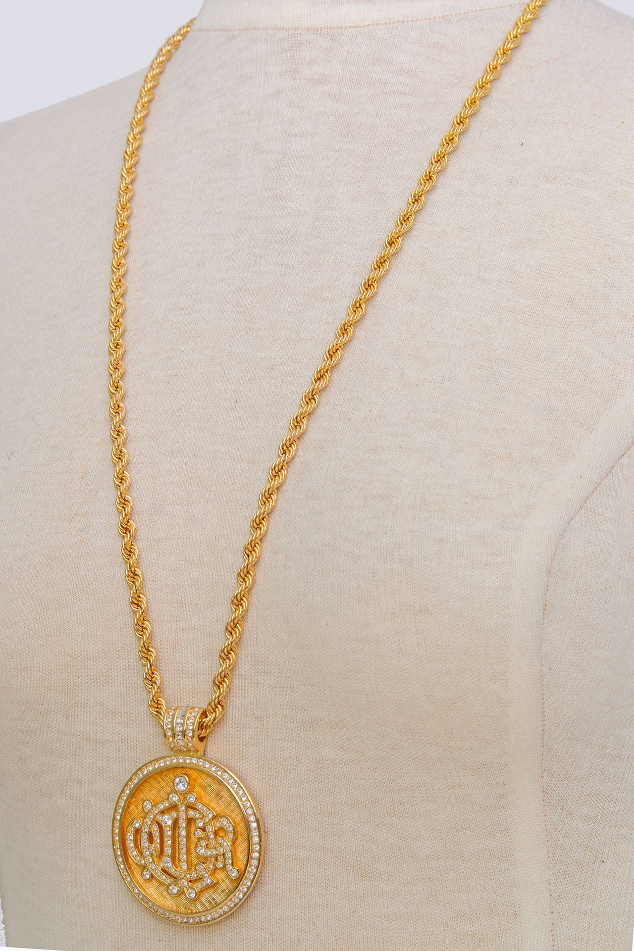 A 1980s Christian Dior gold chain necklace with a large round rhinestone studded pendent with C. Dior imprint on the centre front. The pendent measures 5x5 cm in diameter.

The necklace is stamped: Chr. Dior on the back of the pendent and on the