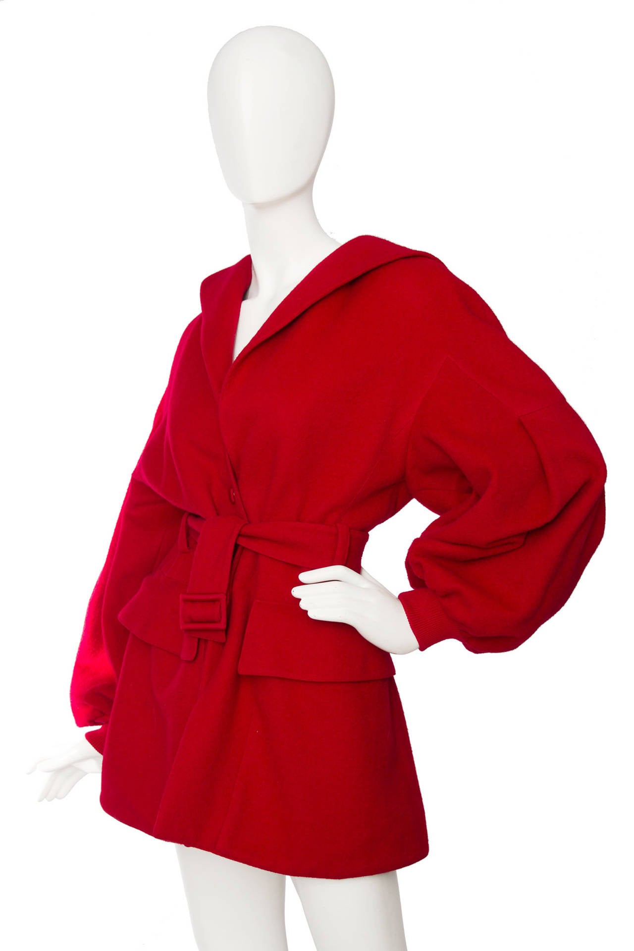 A stunning 1980s Claude Montana bright red hooded wool coat with voluminous sleeves with elasticated cuffs and rounded shoulders. On each side of the hip the coat has two square flap patch pockets. The coat is fully lined and closes in the front