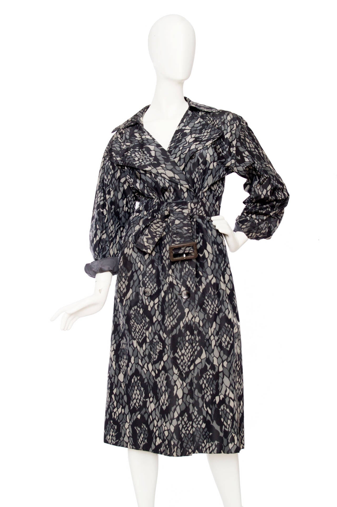 A 1980s Yves Saint Laurent couture silk trench coat with  print in grey hues. The coat has a front button closure, one buttoned cuffs and a wide waist belt in matching fabric and two front pockets. 

The coat is numbered: 59124

The size of the