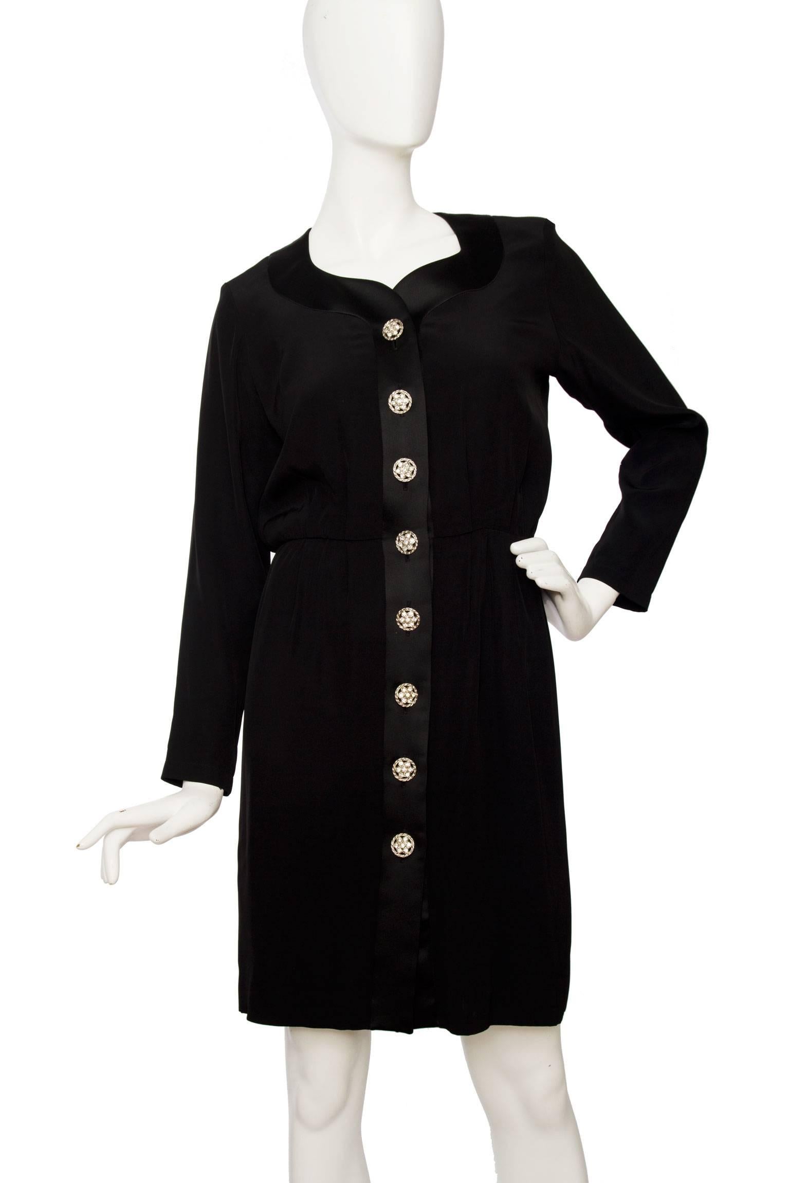A glamorous 1980s Yves Saint Laurent little black cocktail dress, with a narrow waist, long sleeves and a satin trim around the sweetheart neckline and down the front. On the front the dress is embelished with rhinestone studded buttons. The dress
