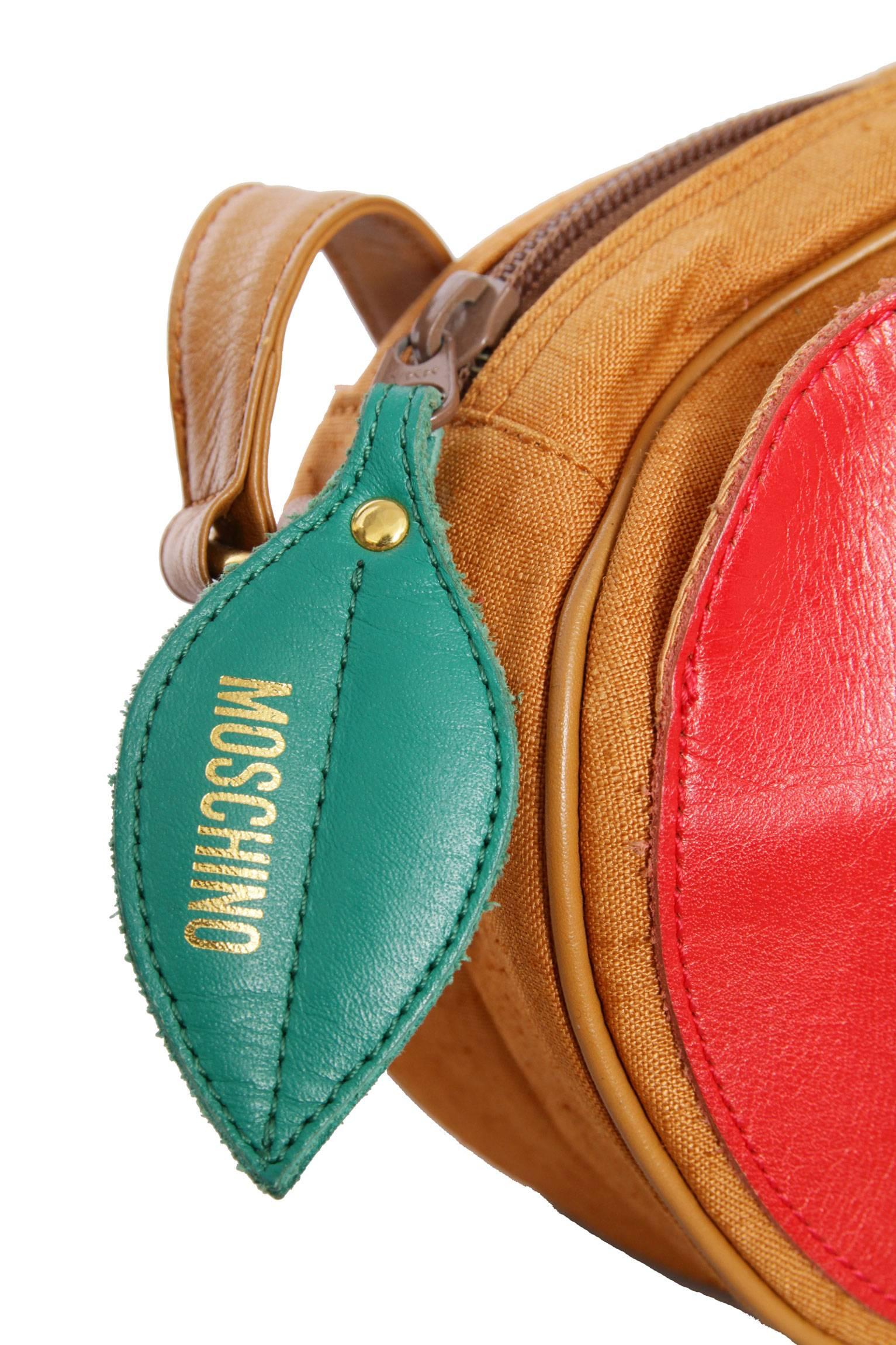 A quirky 1980s Moschino cross body pear shaped shoulder bag made in a light brown colored canvas and a leather strap. The bag has gold hardware and a large green leaf detail attached to the zipper closure, both have been stamped: Moschino.
Inside