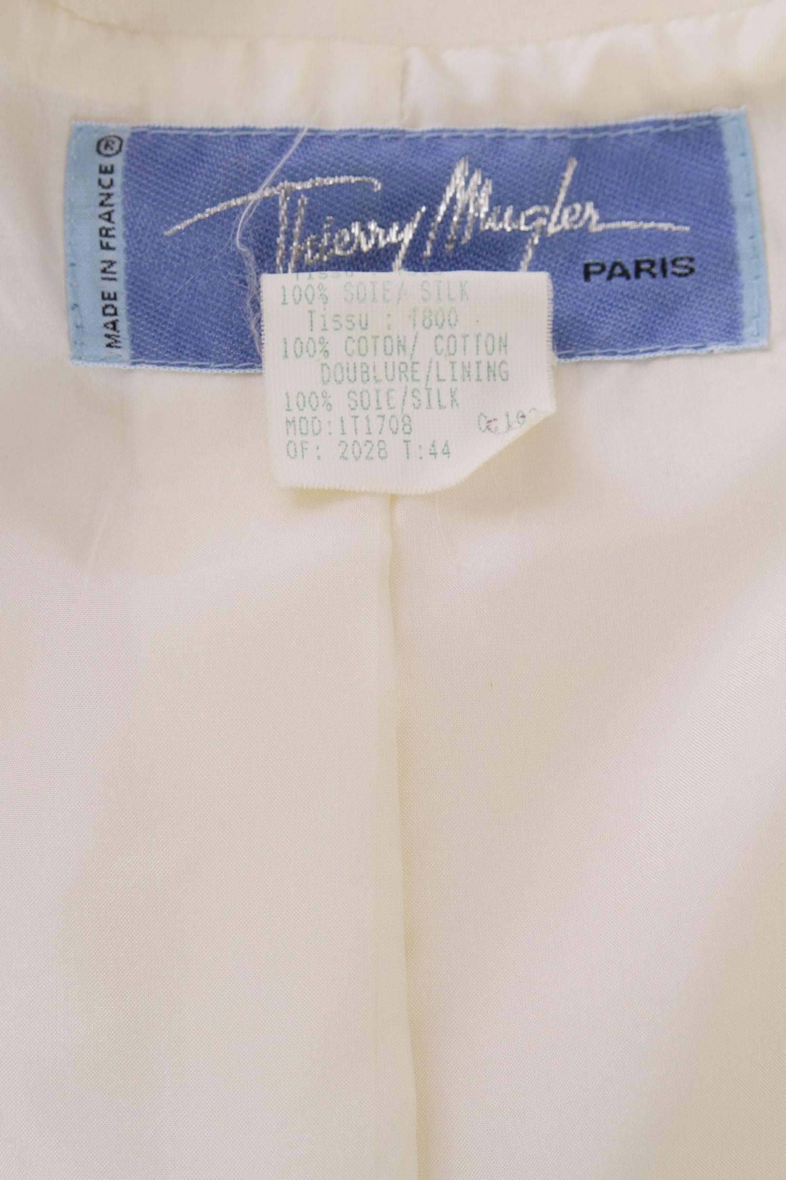 A glamorous 1980s Thierry Mugler off-white silk evening blazer with a fitted waist, shoulder-pads and a single hidden push button closure in the centre front. The blazer is completed by an abstract black cotton velvet trim around the neckline and