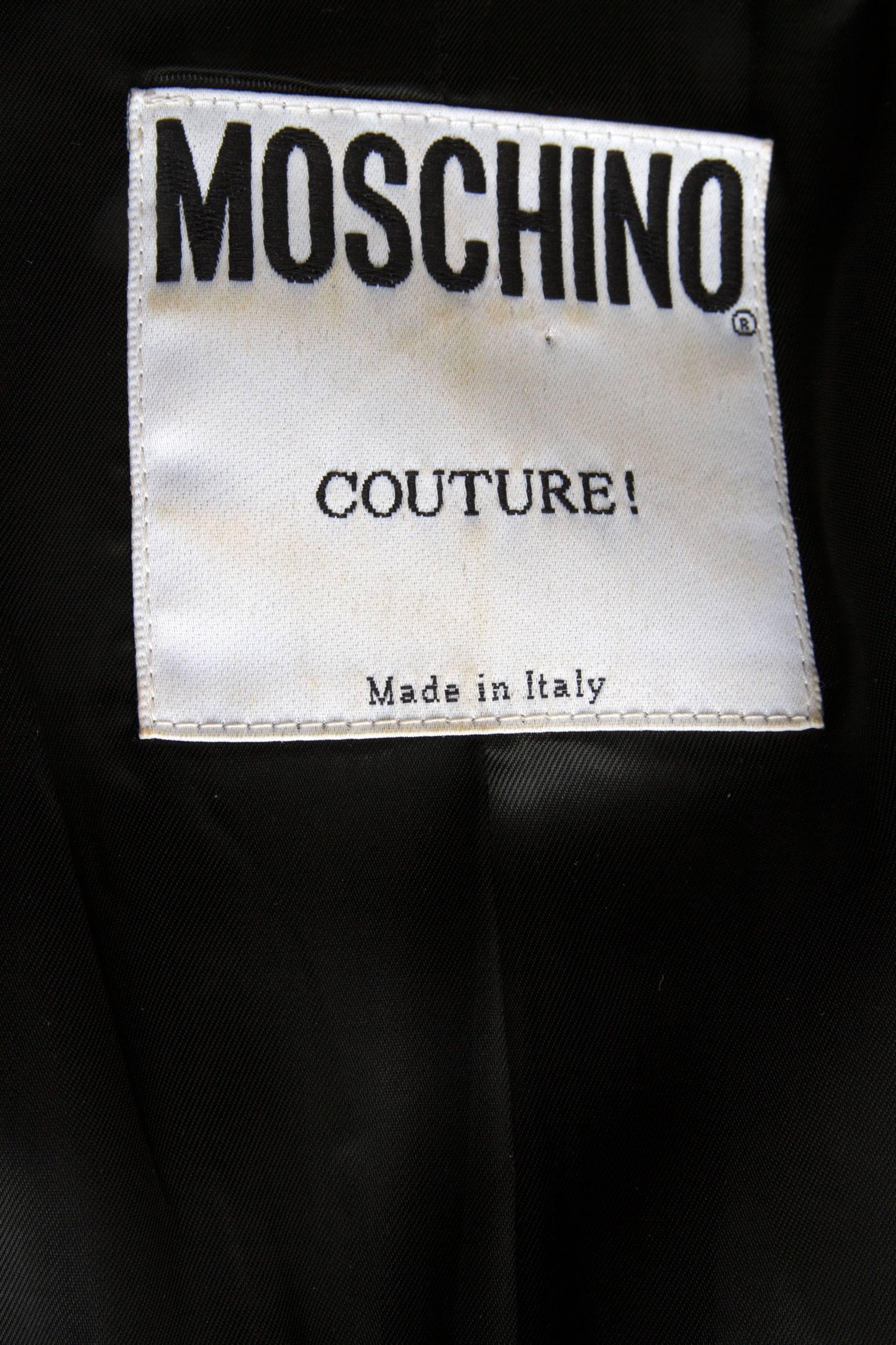 A 1990s black Moschino Couture blazer with a deep round cut front exposing an attached black lace undergarment. The bustier has an oval shape and close in the front with a gold buckle and a silky ribbon that can be tied in front. A flap pocket is