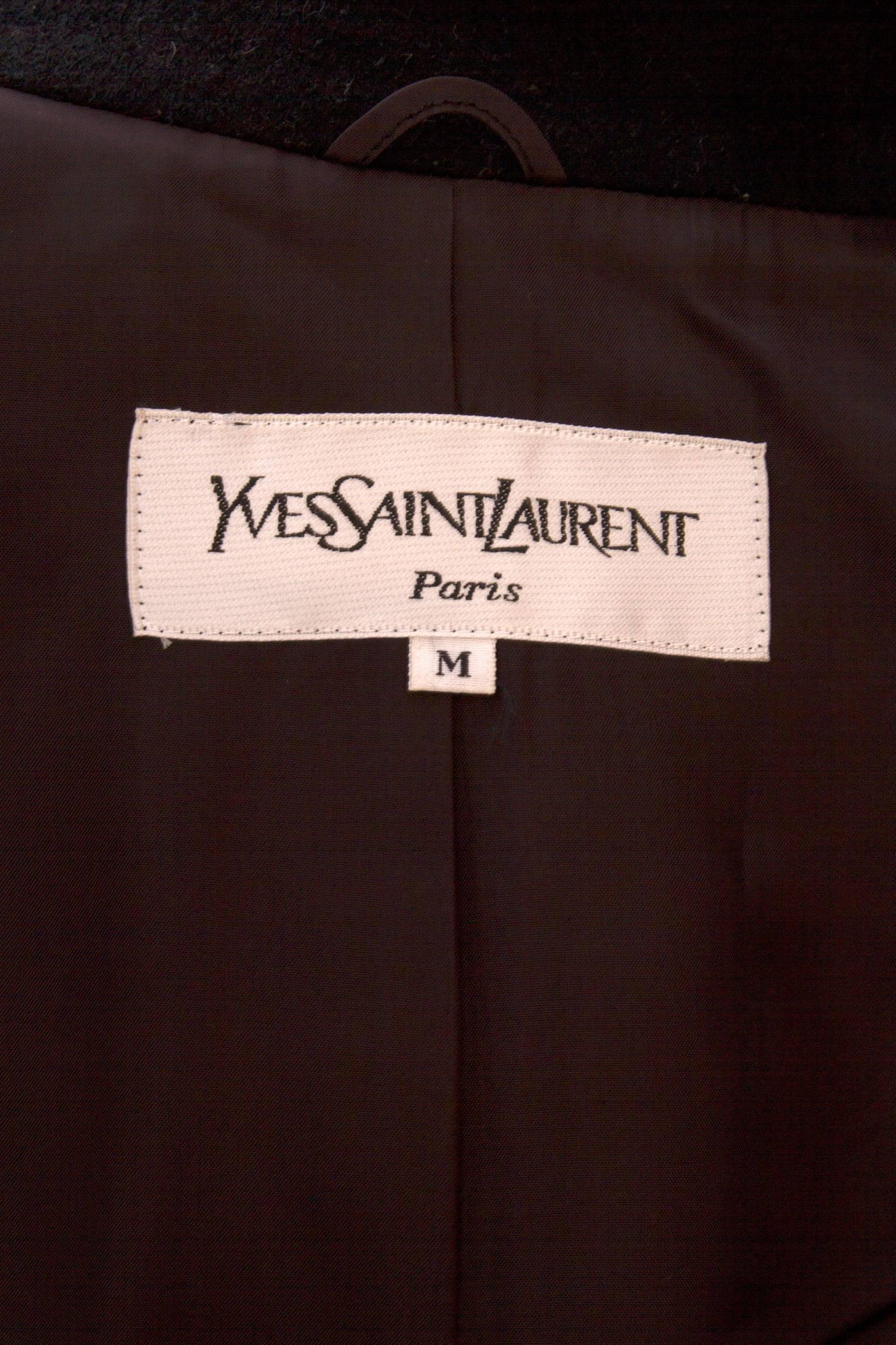 A 1980s black Yves Saint Laurent wool coat with a wide off-white panel down the front. 
The coat has a black stand up collar and buttons down the front with large black buttons standing as a delicate contrast to the white panel. 
The long sleeves