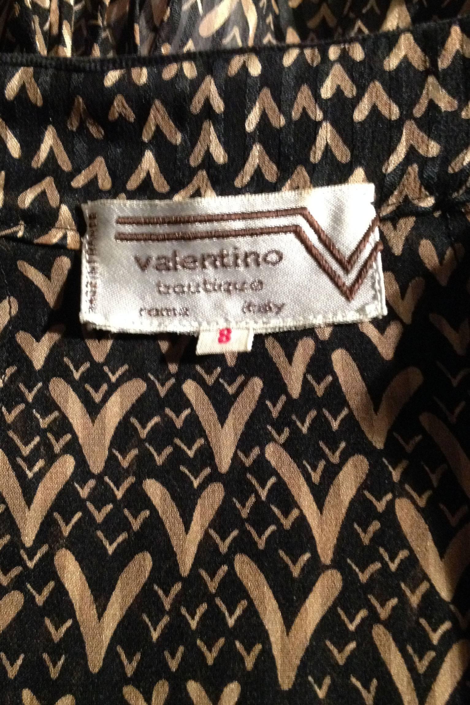 A 1980s Valentino sheer silk blouse with V-print in a complimenting gold tone. The blouse have an adjustable collar that can be worn standing up exposing a black velvet trim or as a a round collar in matching silk fabric. Around the waist a draw