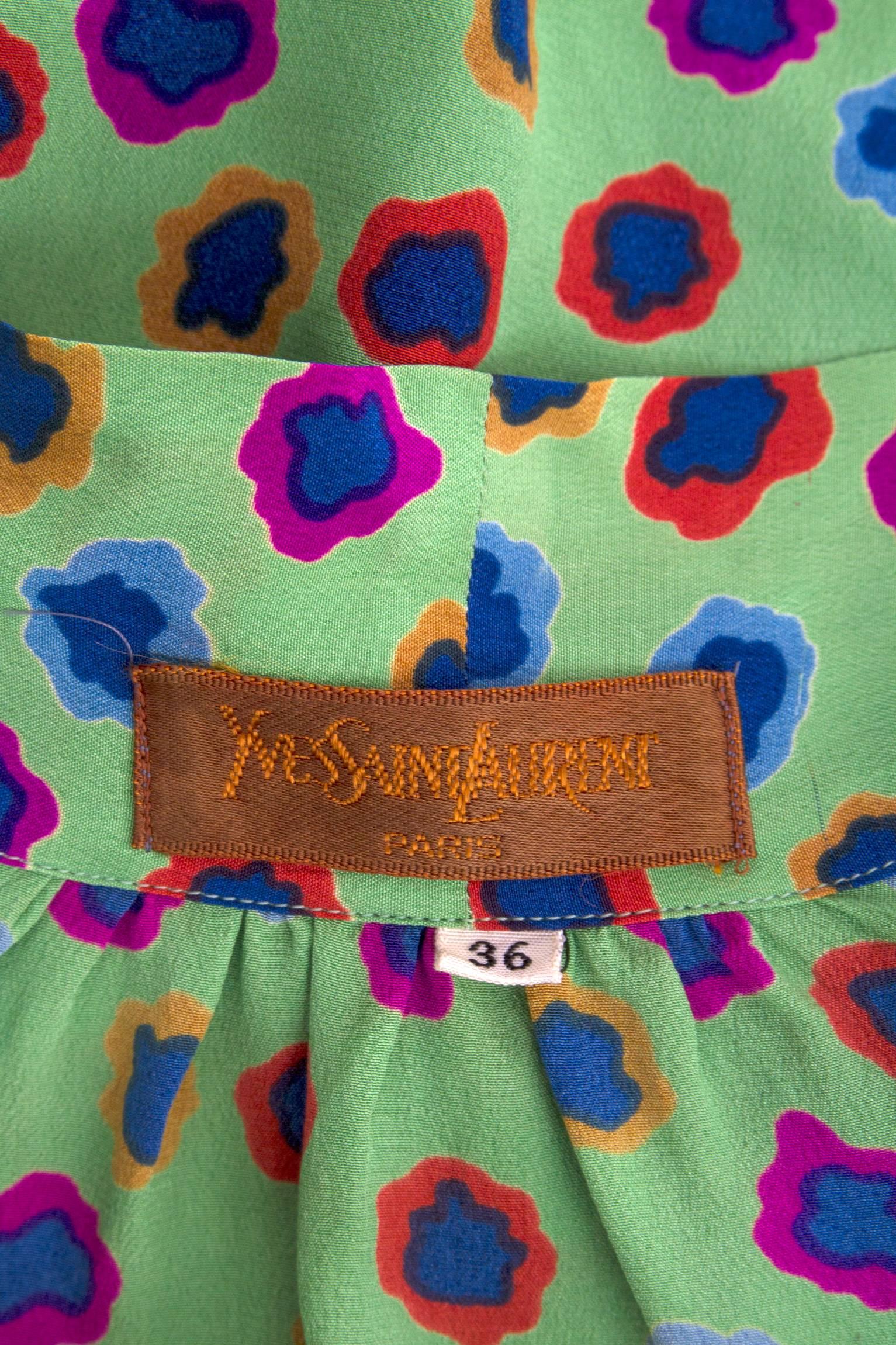 A fun 1980s Yves Saint Laurent pussy bow silk blouse with a hidden front buttoned closure and one buttoned cuffs. The blouse has an abstract floral print in bright yellow, pink, orange and blues, which stand as a complimenting contrast to the light
