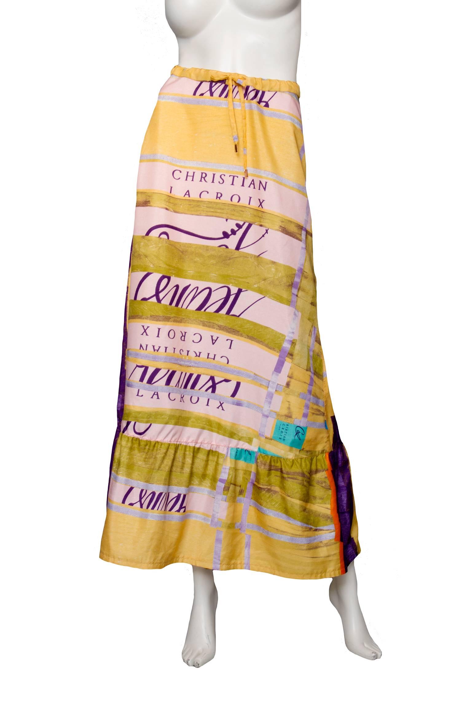 A graphic 1990s Christian Lacroix peasant silk skirt with a ruffle hemline and colorful print held in a bright yellow, blue and purple color scheme with purple Lacroix insignias. The skirt features both a draw string closure at the front and a