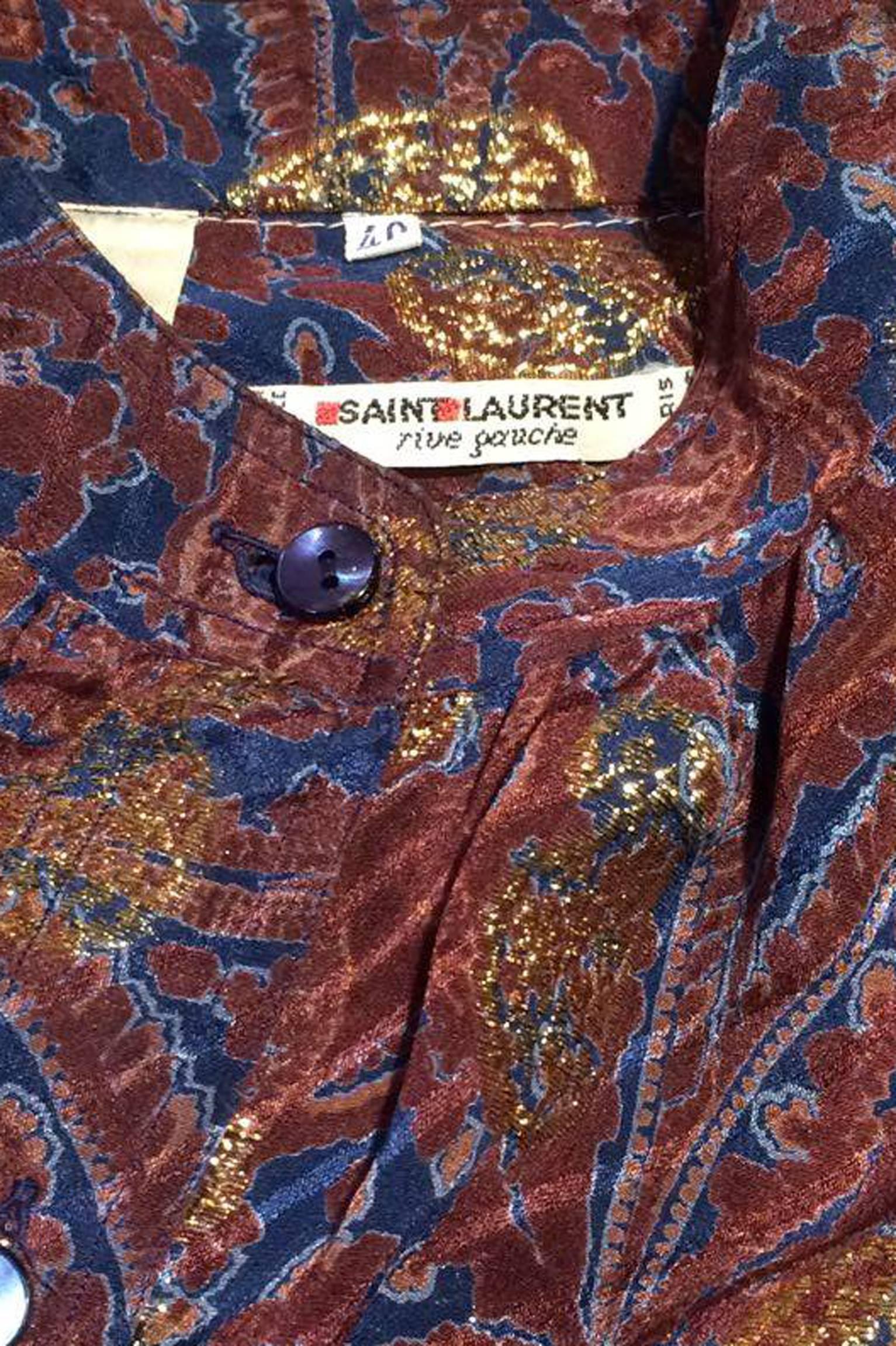 A ravishing 1970s Yves Saint Laurent Rive Gauche bordeaux silk blouse with a blue and gold lurex paisley print. The blouse has a front button closure and two-button cuffs. 

The size of the blouse corresponds to a modern size Extra-Small.
