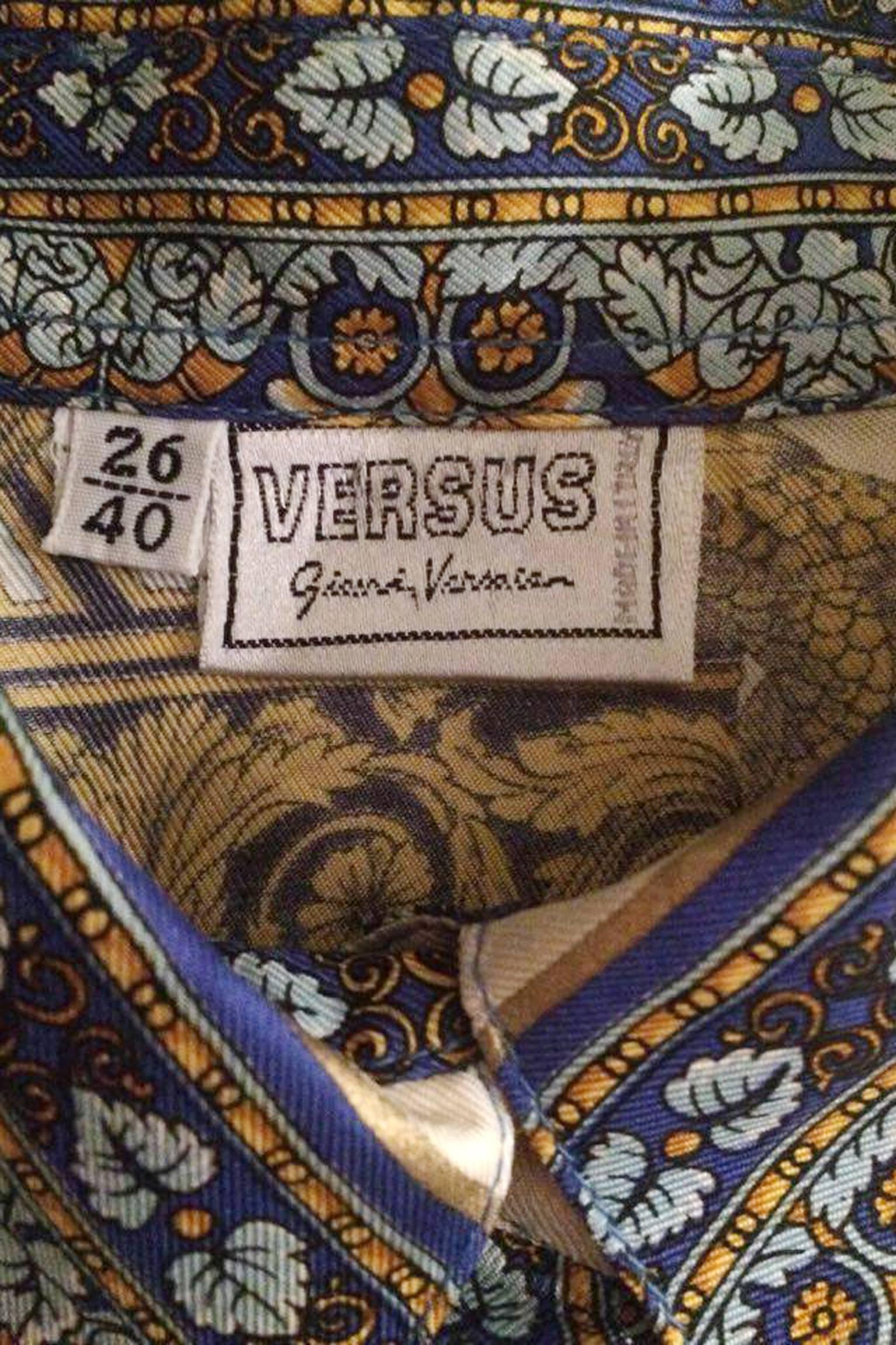 A colourful 1990s Versace silk shirt with a detailed, Italian inspired print of urns and a large emblem on the back. The white shirt has a wide colourful florel trim and the motifes are all in a colour scheme of gold, bronze, blue, purple and