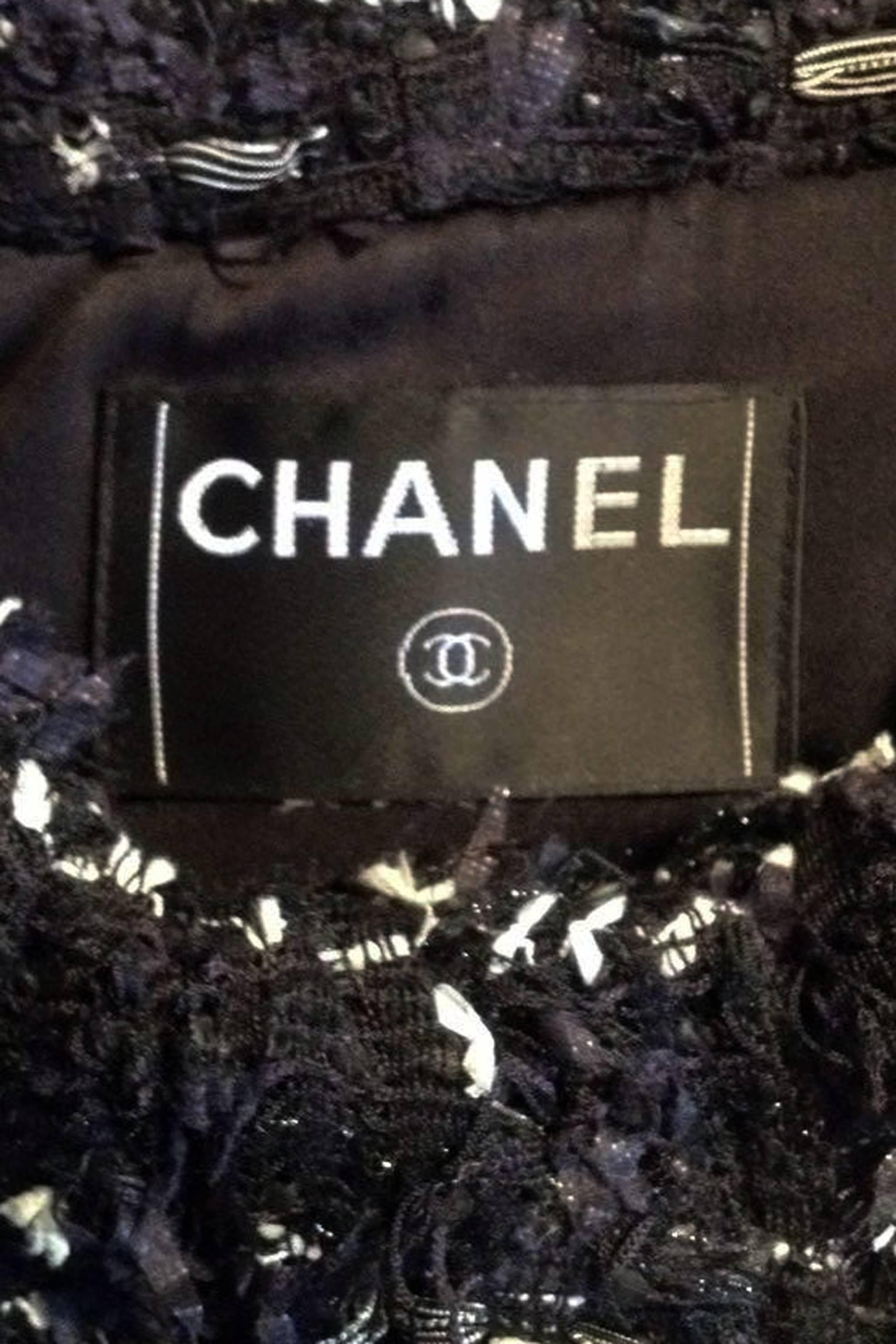 A black & whiteChanel boucle jacket with three-quarter length sleeves, a large ruffled collar, and four strategically placed patch pockets. The jacket is fully lined and closes in the front with four black novelty bottle top buttons market 