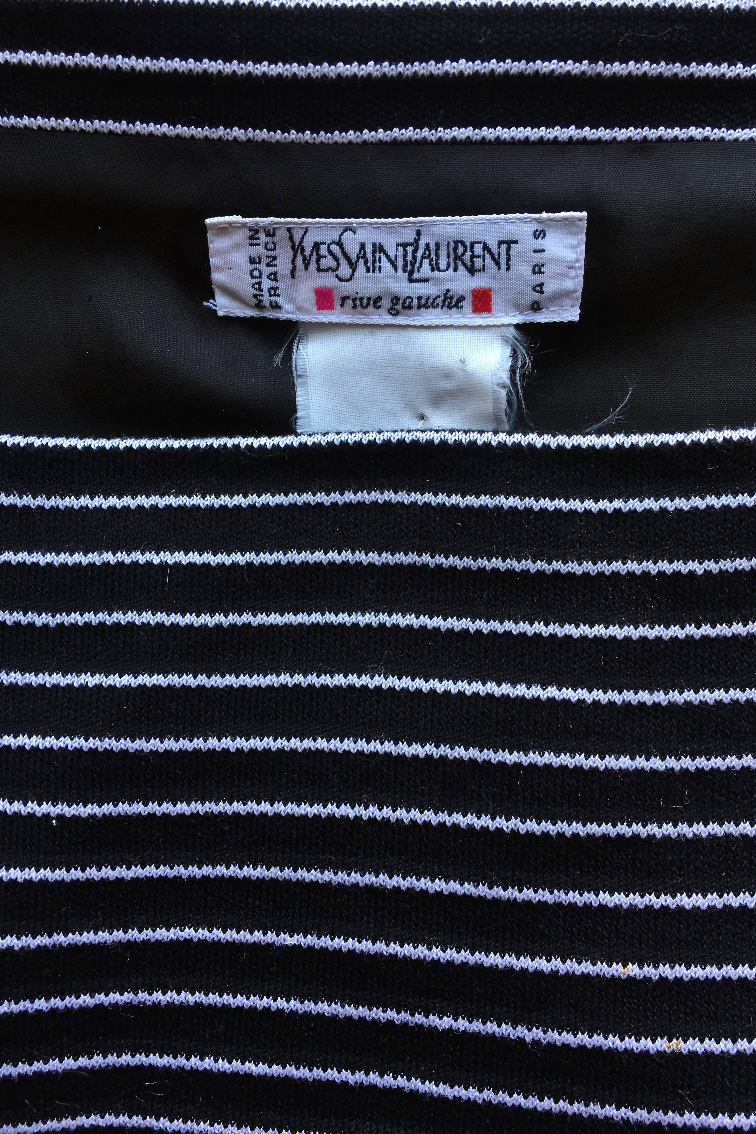 A monochrome 1980s Yves Saint Laurent Rive Gauche stiped wool day dress with black and white vertical stripes. The dress has short sleeves, a square neckline and a double-breasted closure which can be opened on both sides. 

The size of the dress