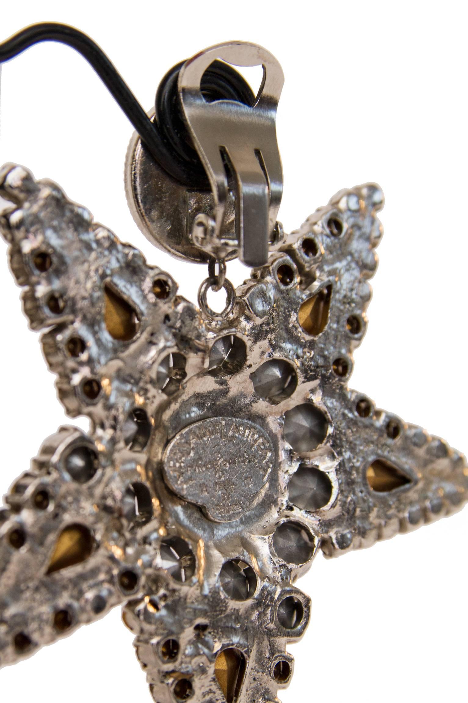 A pair of 1980s sparkling rhinestone studded Yves Saint Laurent Rive Gauche clip-on earrings consisting of a large rhinestone center with a large star-shaped pendant. 

The earrings are stamped: Yves Saint Laurent, Rive Gauche, Made in France

The