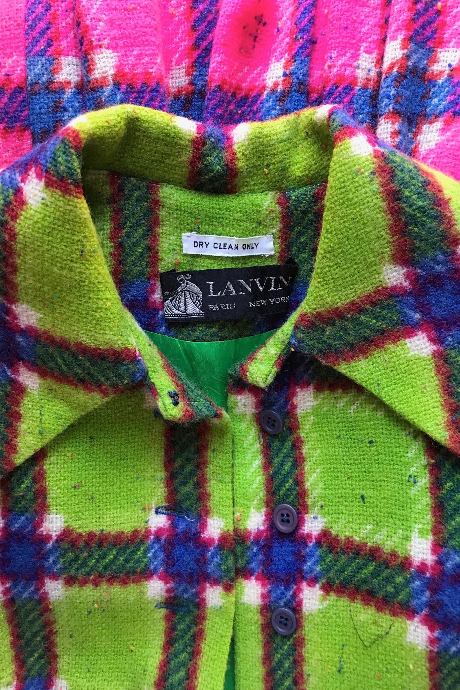 A colorful 1970s Lanvin bright pink and lime green tartan wool coat dress consisting of a fitted top and floor-length skirt. The dress has a full front button closure and a matching slim waist-belt. The bold tartan is completed with blue and white