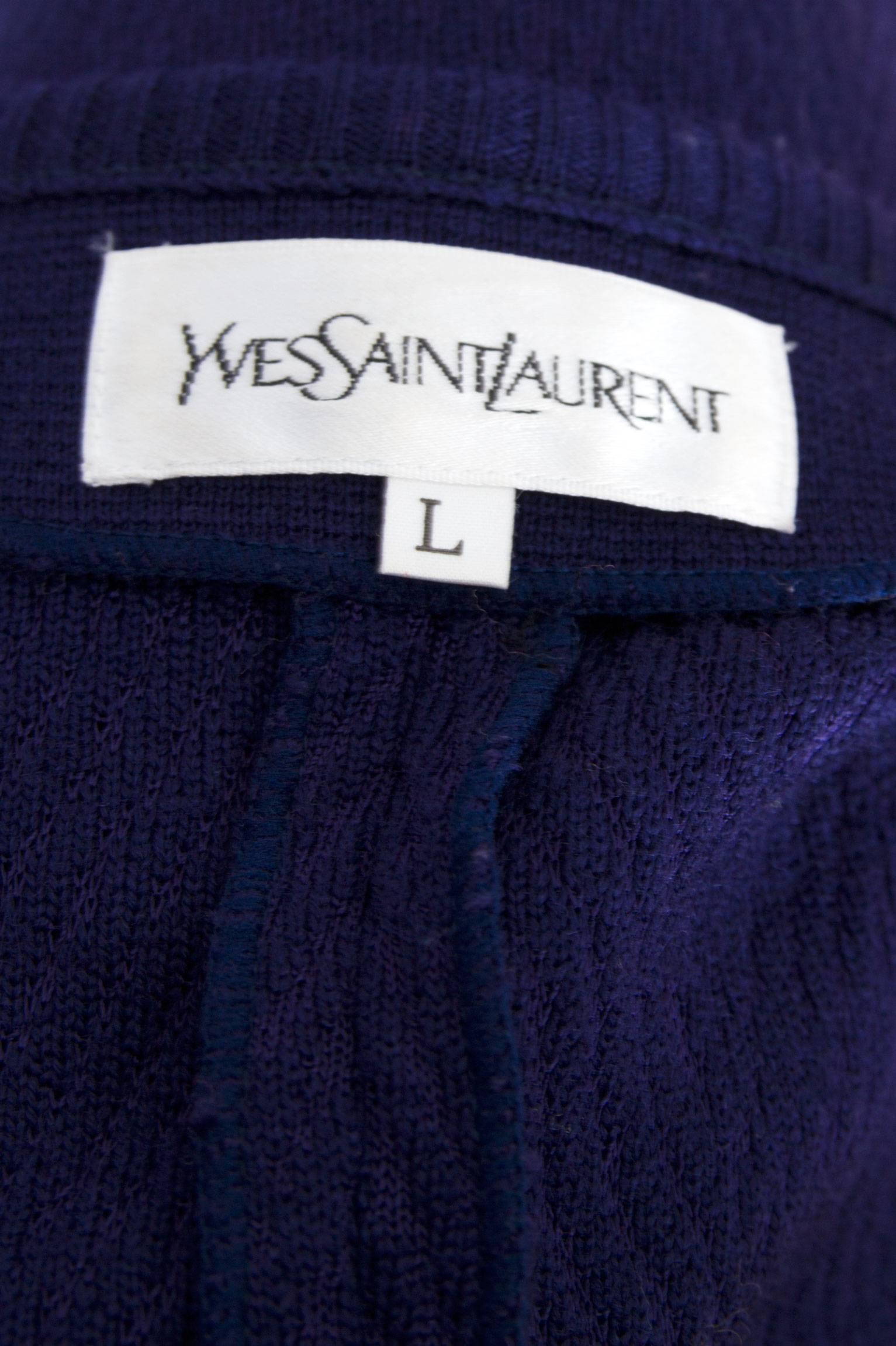 A 1980s Yves Saint Laurent purple knitted Cardigan with long sleeves and a round neckline. The dress buttons down the front, has faux flap pockets situated on each hip and a three button detail on the cuff. All the gold buttons have an YSL logo