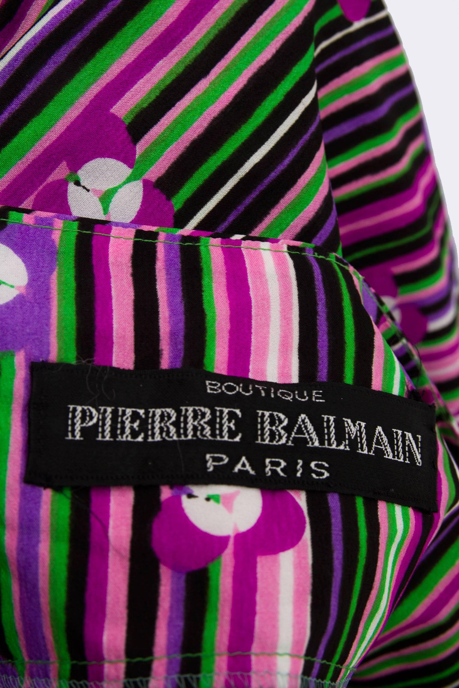 A flirty 1970s Pierre Balmain silk brightly colored silk dress with a floor-length a-line skirt and a v-neckline. The top of the dress has an illusionist wrap front and a three button detail on the left side of the sleeveless shoulders. Asymmetrical