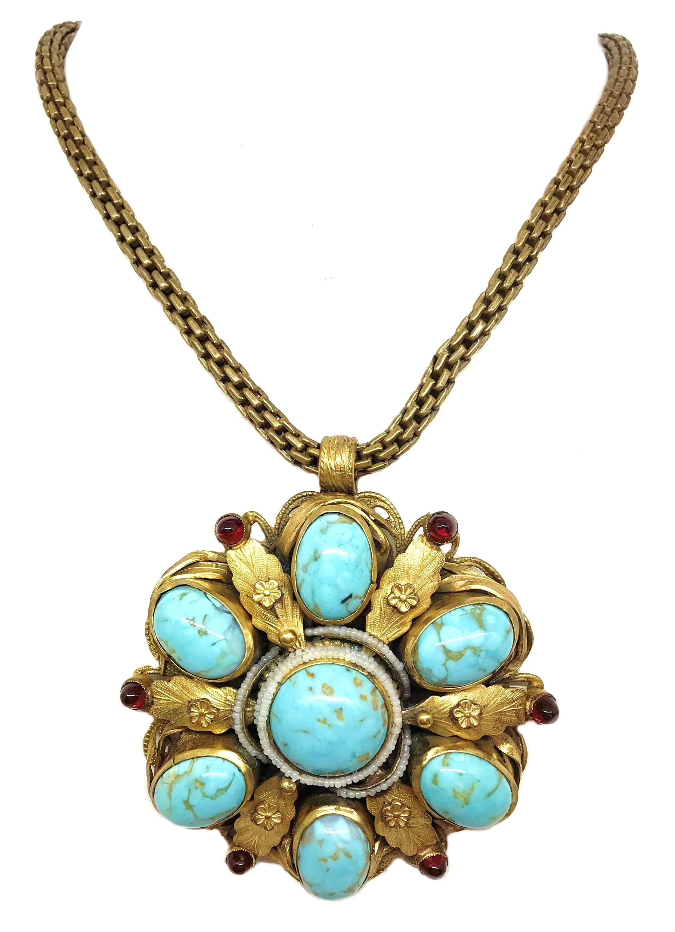 Circa 1940s gold tone metal chain necklace with a large, ornate pendant bezel set with oval and round turquoise glass cabochons. The pendant is  embellished with small glass pearl beads and red glass cabochons and measures 3.25