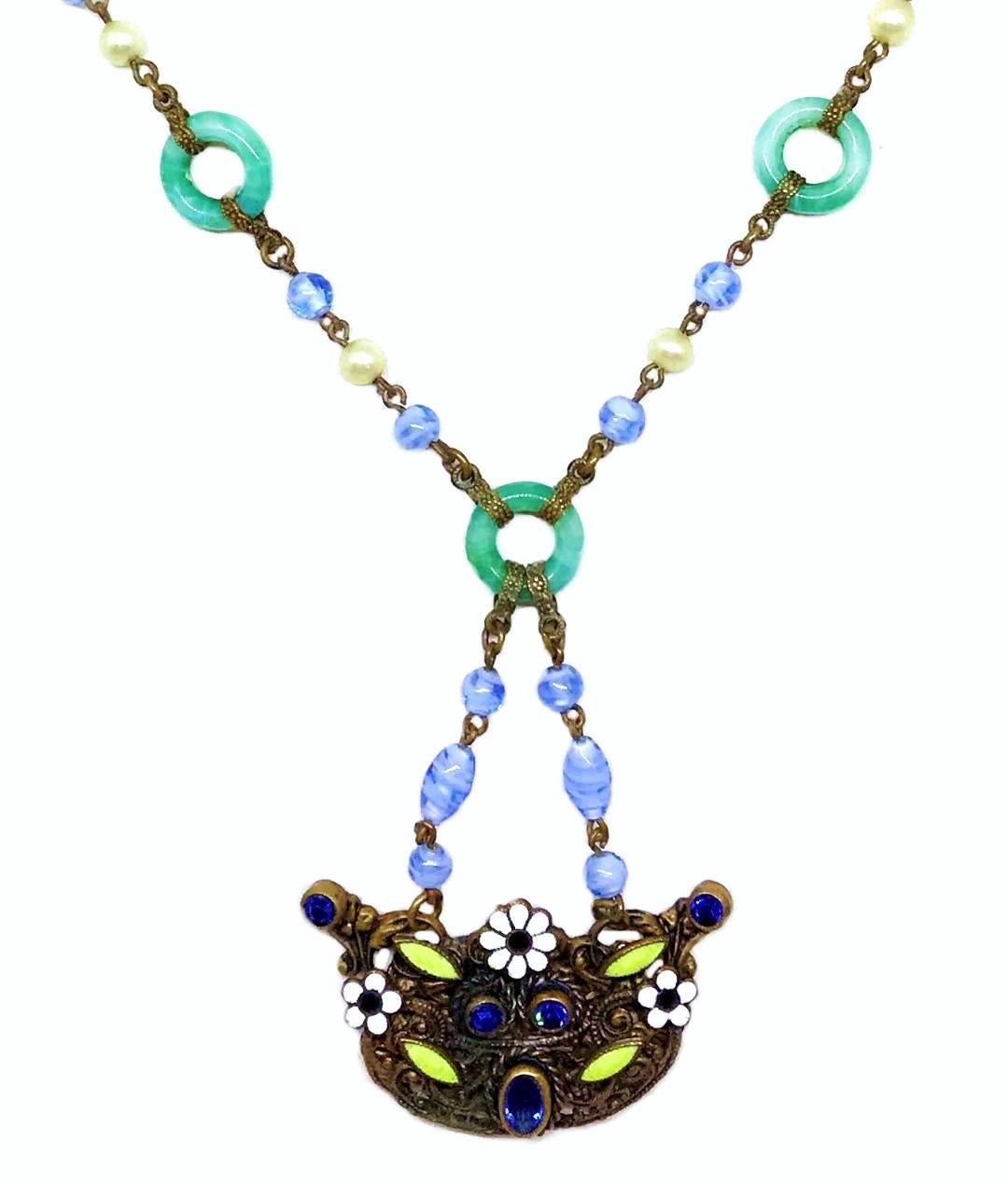 Circa 1920s Czech blue and green glass bead necklace with green glass circles and fancy brass findings. The ornate brass pendant is bezel set with dark blue faceted glass stones and embellished with enameling.  The pendant, including the bead chain