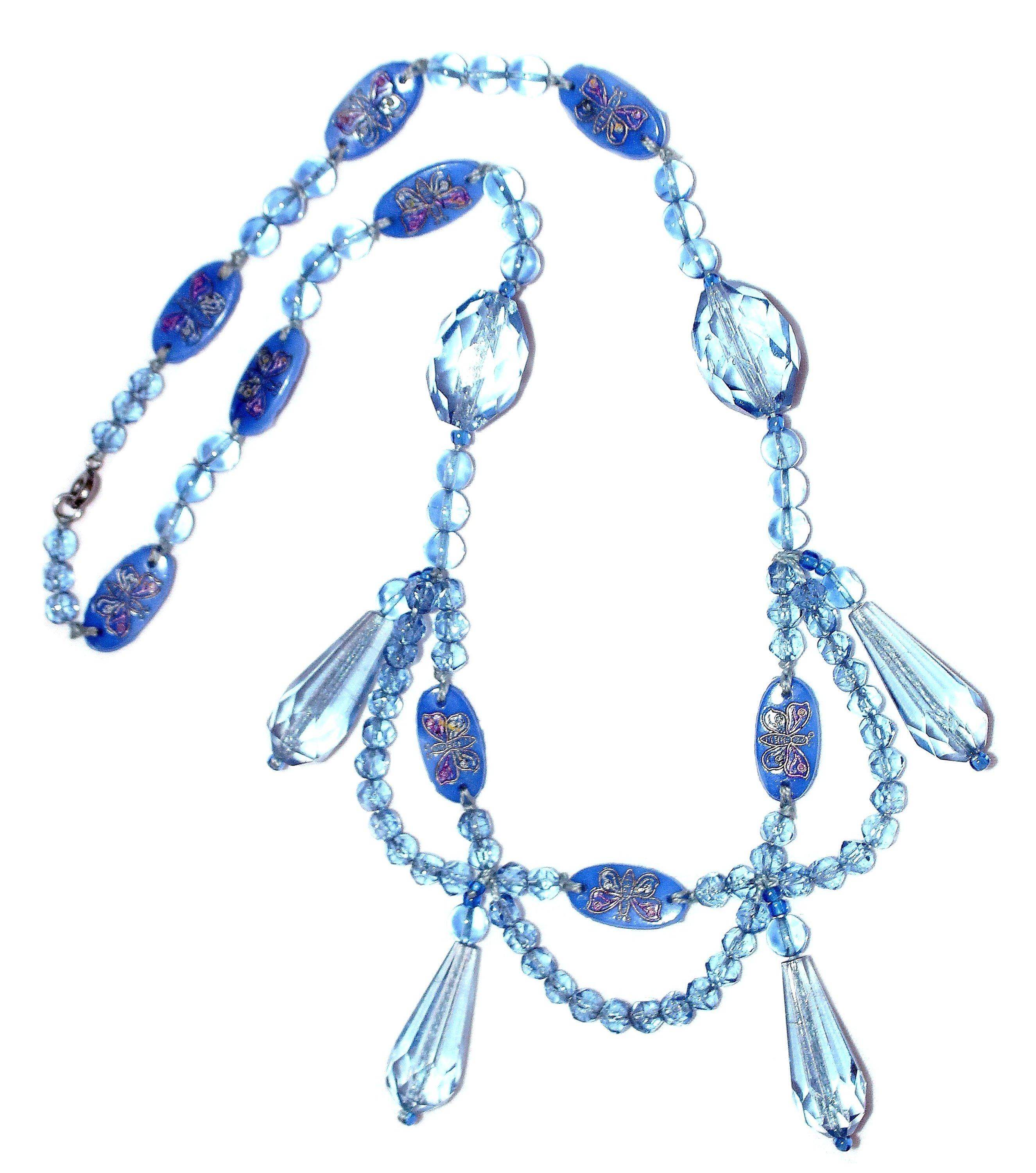 Circa 1920s to 1930s light blue faceted and smooth glass bead swag design necklace.  It is embellished with faceted drops and interspersed, blue glass oval plaques hand painted with butterflies.  The necklace is 20