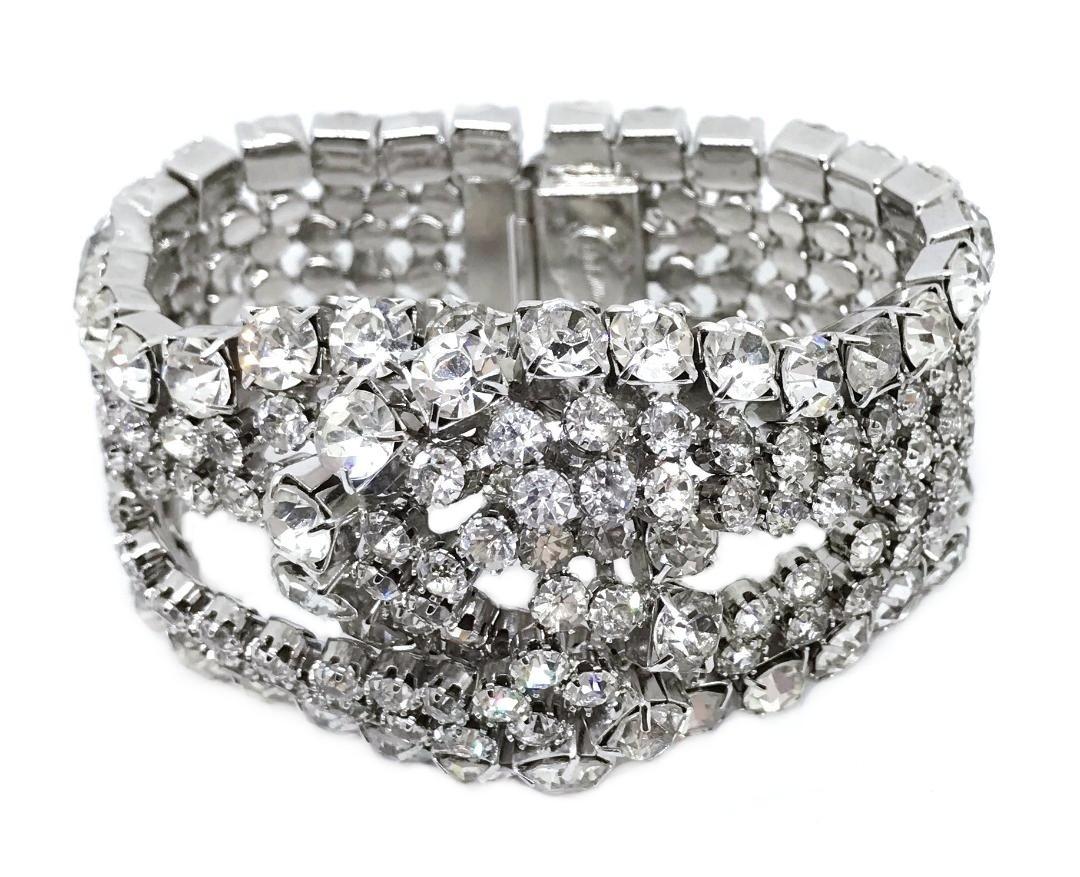 Circa 1960s William deLillo wide, rhodium plated silver tone metal cocktail bracelet with an intertwined loop design.  It is prong set with large clear faceted glass stones. This large statement bracelet is from the designers collection.  The