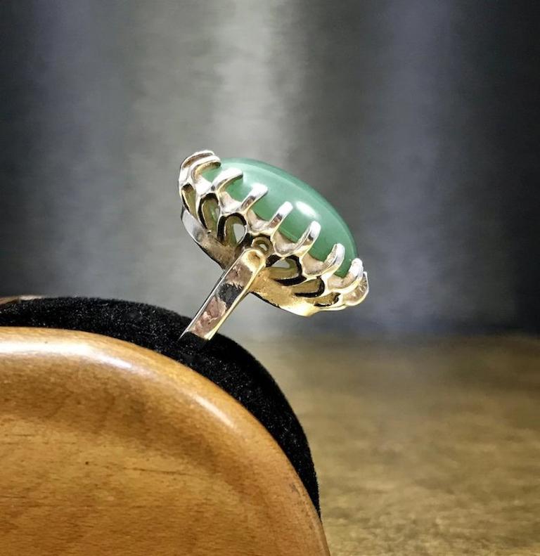 This green vintage ring dates back to the 1960s, Mid Century - Minimalist era, is crafted with fine 950 sterling silver, and features an oval cabochon cut green jadeite jade stone, and a unique, artisan crafted, multi prong design. This unique green