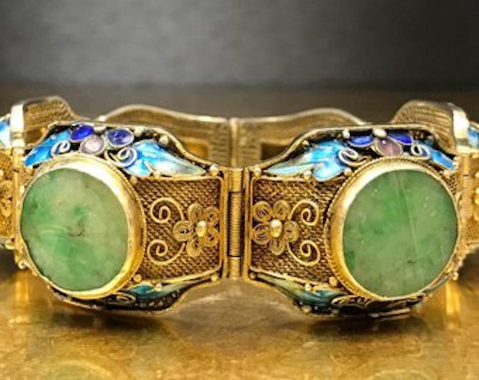 This antique Art Nouveau bracelet  is crafted with gilded - gold washed sterling silver and features four round, carved green jadeite jade stone accents, intricate filigree detailing, vibrant aqua blue, blue, royal blue, and purple enameling, and a