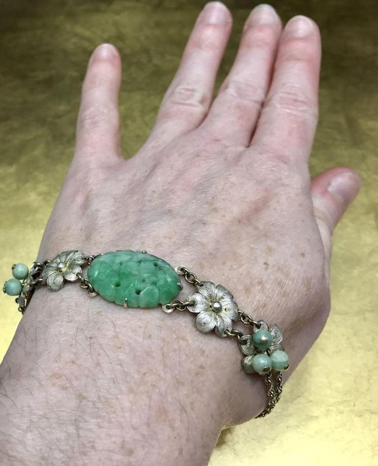 This vintage floral bracelet dates back to the 1920s the late Art Nouveau - early Art Deco eras. Crafted with 925 sterling silver, this unique green bracelet features a large, oval shaped, carved jadeite jade accent, six tiny jadeite jade beads, and