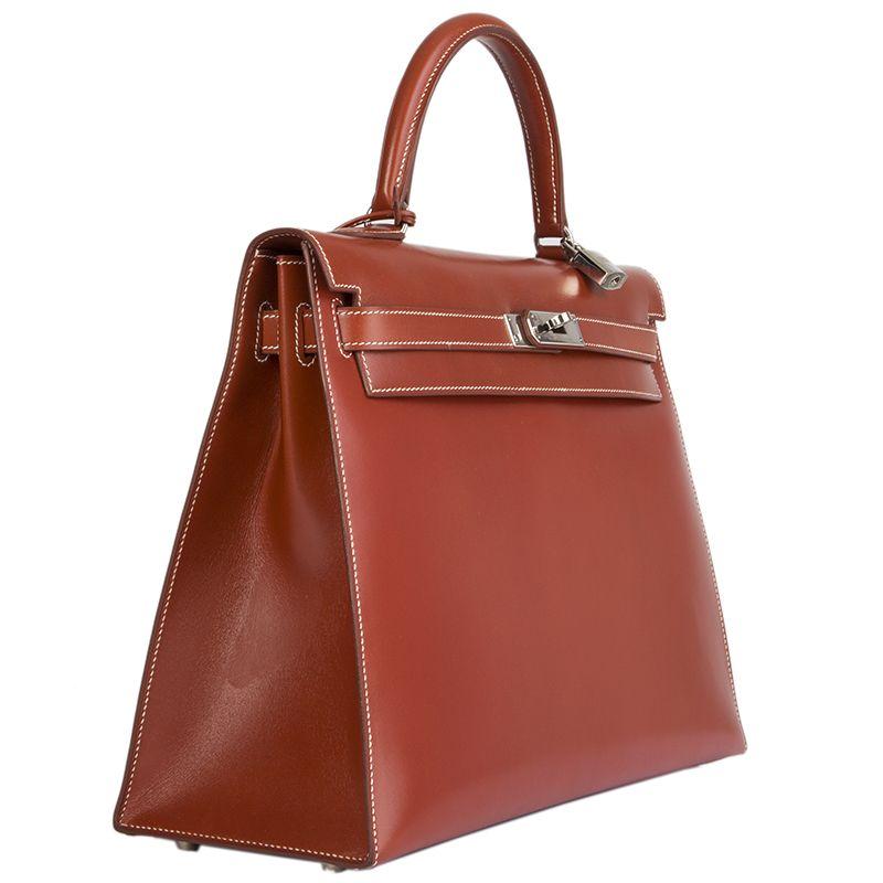 Hermès 'Kelly I 35 Sellier' Bag in brique (brick-red) veau box leather with contrasting white stitches. Lined in chevre (goat skin) with two open pockets against the front and a zipper pocket against the back. Is in virtually new condition with