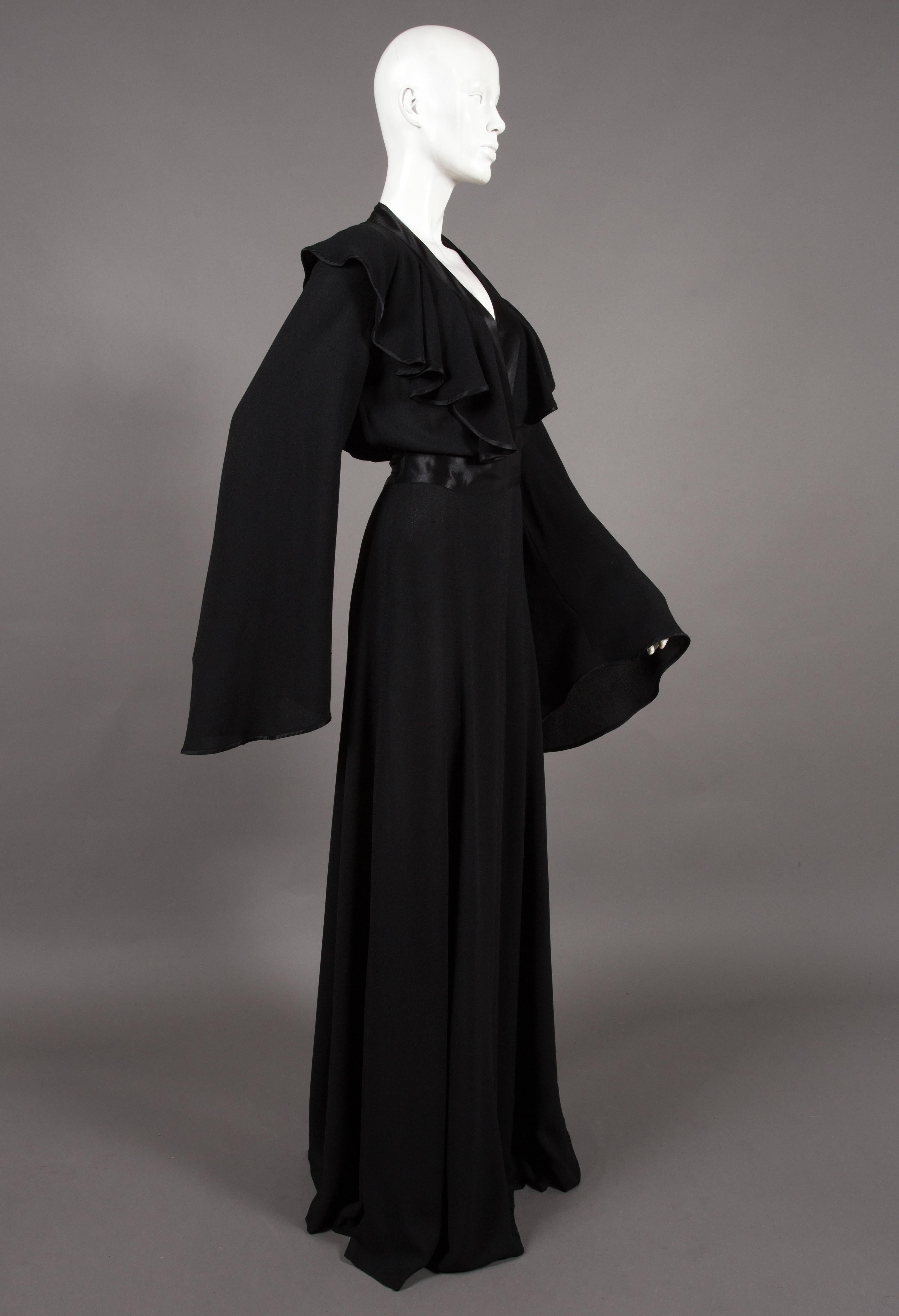 Rare Ossie Clark black moss crêpe wrap around evening dress, circa 1970, printed with the Ossie Clark couture label, size '12', with stain top stitched lapels and satin sash, full bell sleeves and leg slit.


Size: 
Shoulder to shoulder - 18