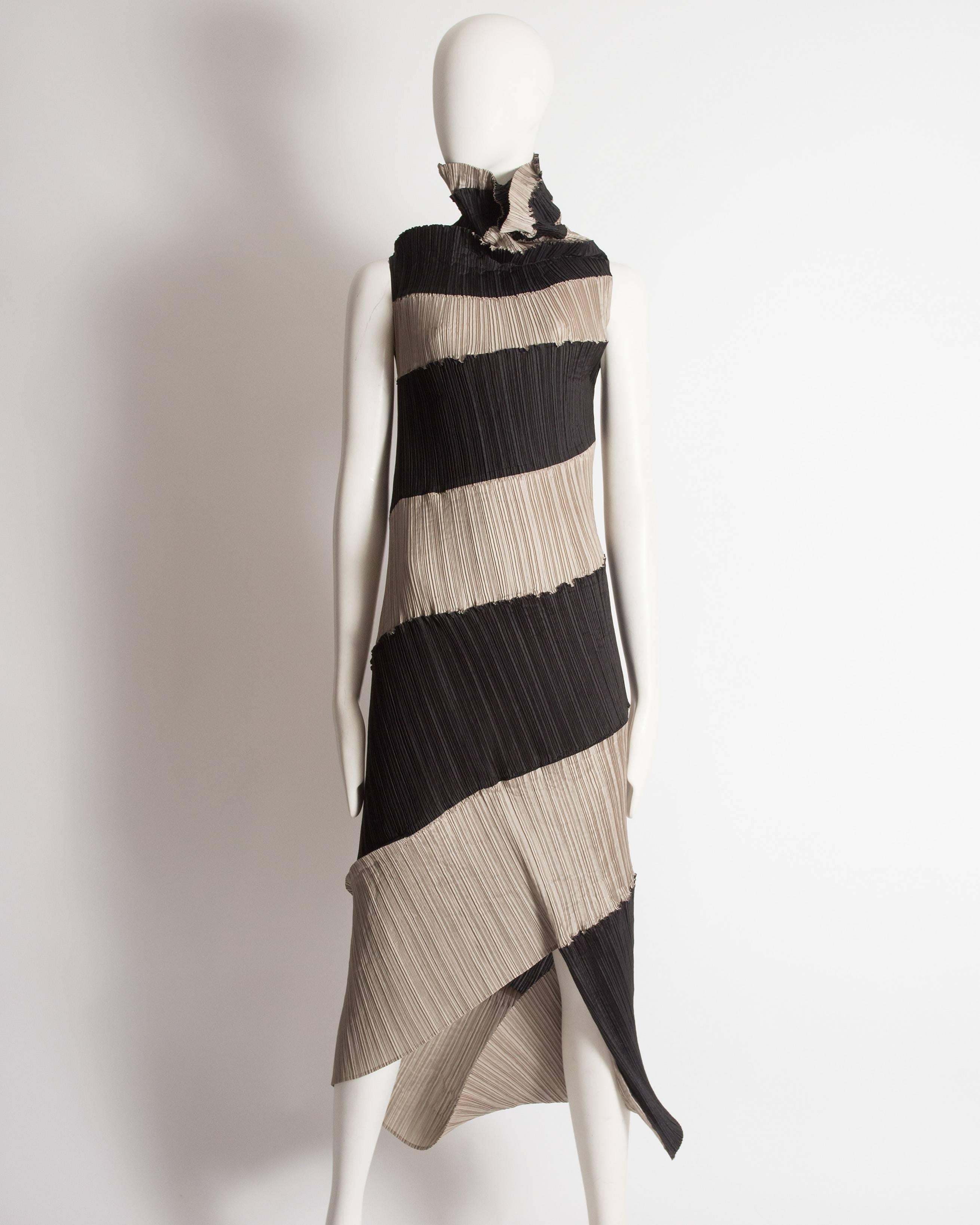Issey Miyake striped evening dress constructed in gray and black pleated polyester with high cowl neck and an asymmetric hem.

Circa 1990-1999