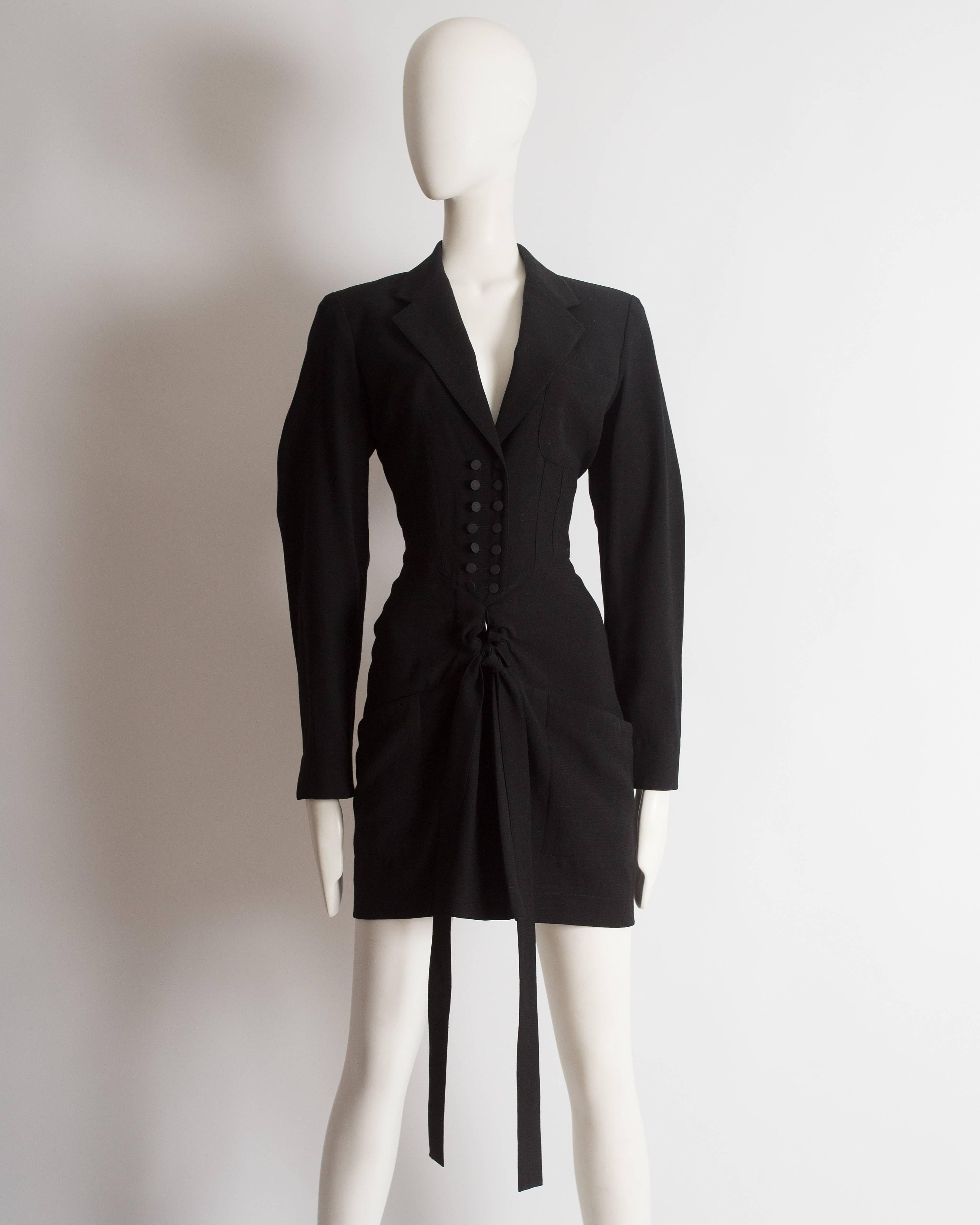 Rare Alaia black wool mini dress with a drawstring fastening, two front pockets, pointed collar and double button closures.

Autumn Winter 1988