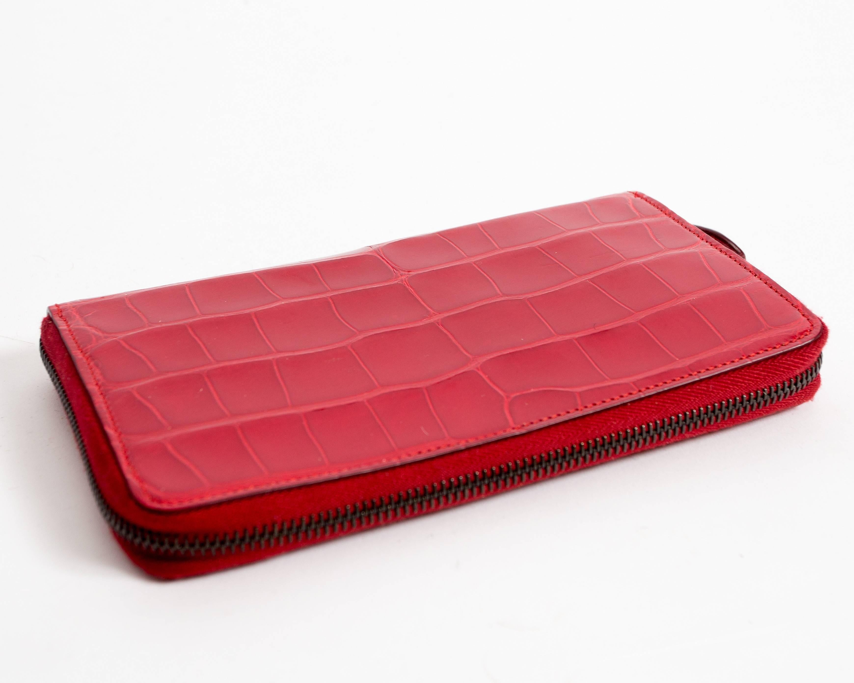 Red patent leather croc-embossed wallet from Alaia. The wallet has a gunmetal zip closure, tan leather lining. Two large compartments, an internal zipped pocket, and 6 card slots. 