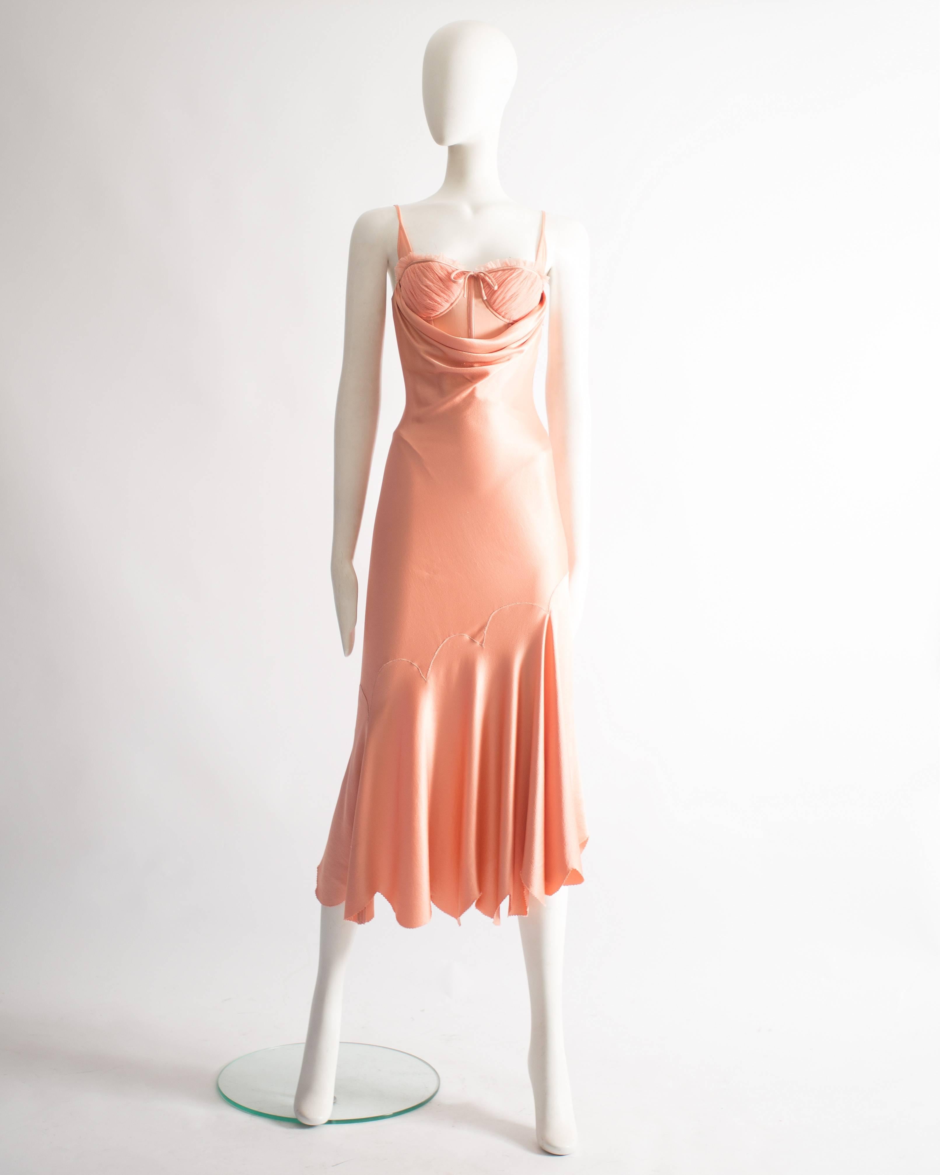 A bias cut evening dress in pale pink silk. Scalloped hemline, internal leotard with boning and pleated tulle bra, partially exposed from the draped neckline at the front and back. From the Alexander McQueen 'Deliverance' Spring-Summer 2004 runway