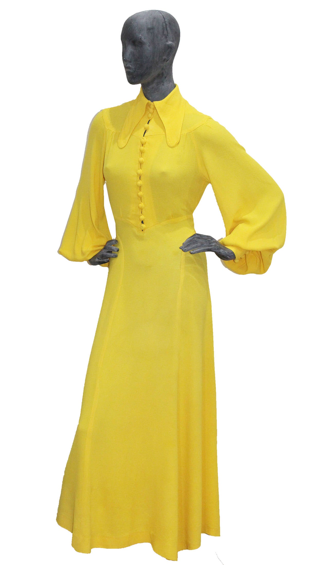A 1975 brilliant yellow brilliant yellow moss crepe evening dress by Ossie Clark for Radley. Long curved collar, button-fronted bodice ending at the waist, love ribbon that ties to rear waist.

Sizing: This dress could fit anyone between a UK size