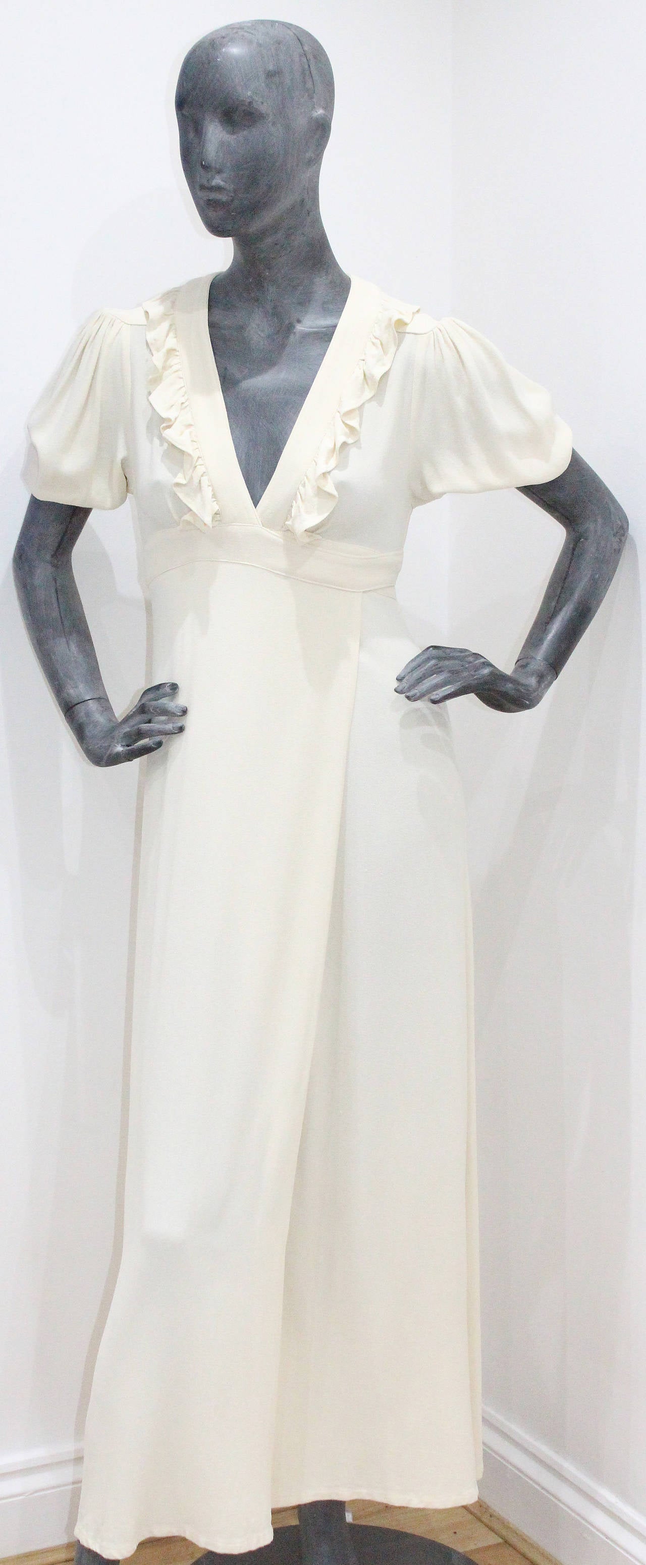 A beautiful ivory wrap dress by Ossie Clark. This design is timeless and chic. The dress has a v-neck plunge with a ruffled trim, a wrap design which ties as a bow to the rear, a central leg slit, structured 1940s inspired shoulder and draped puff