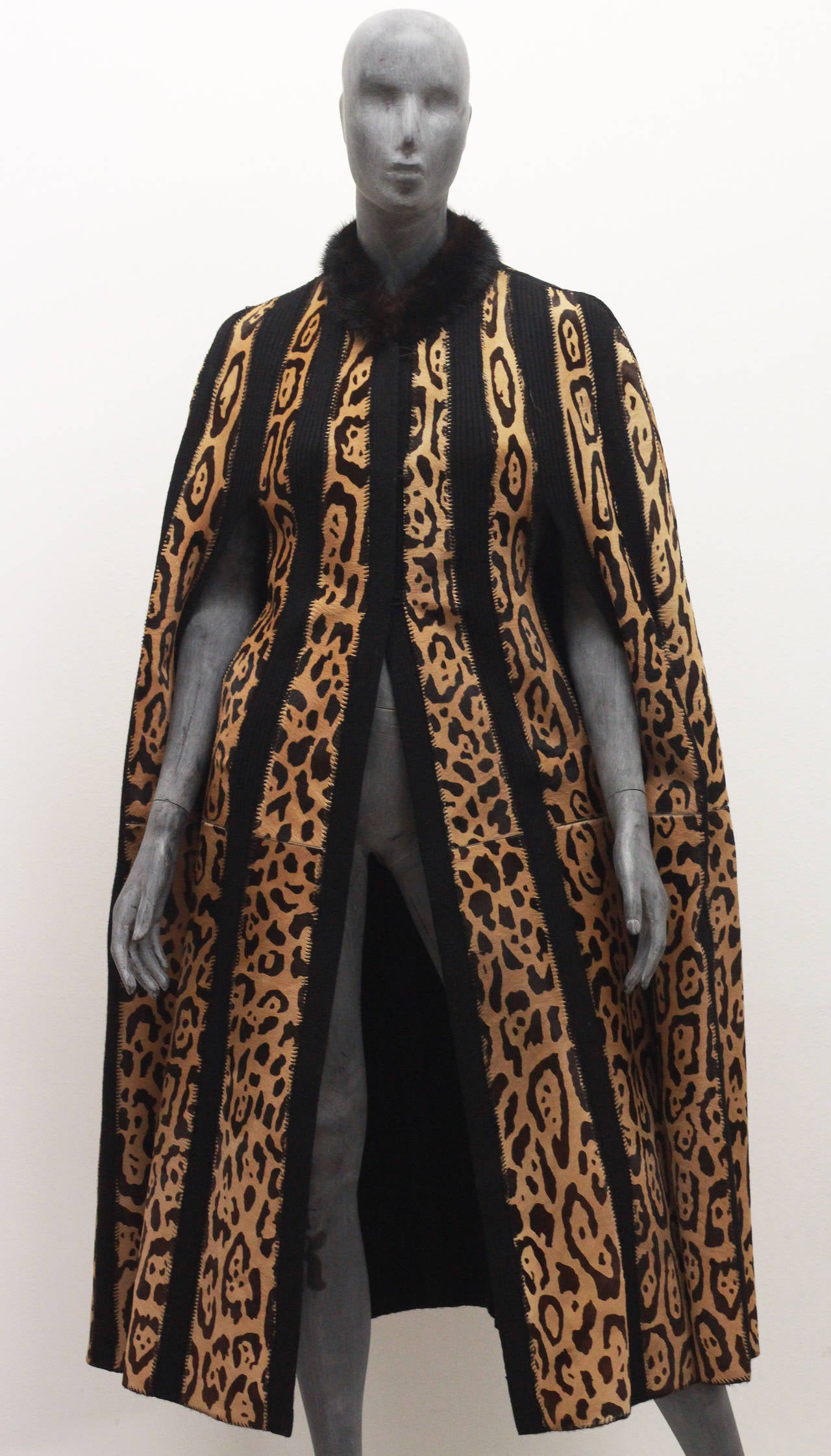 A full length cape by Beltrami from the 1980s. The cape has panels of pony skin in a leopard print and panels of a heavy black knit in between. The collar is made from a brown mink fur. The cape also features to arm slits to allow movement. 

One