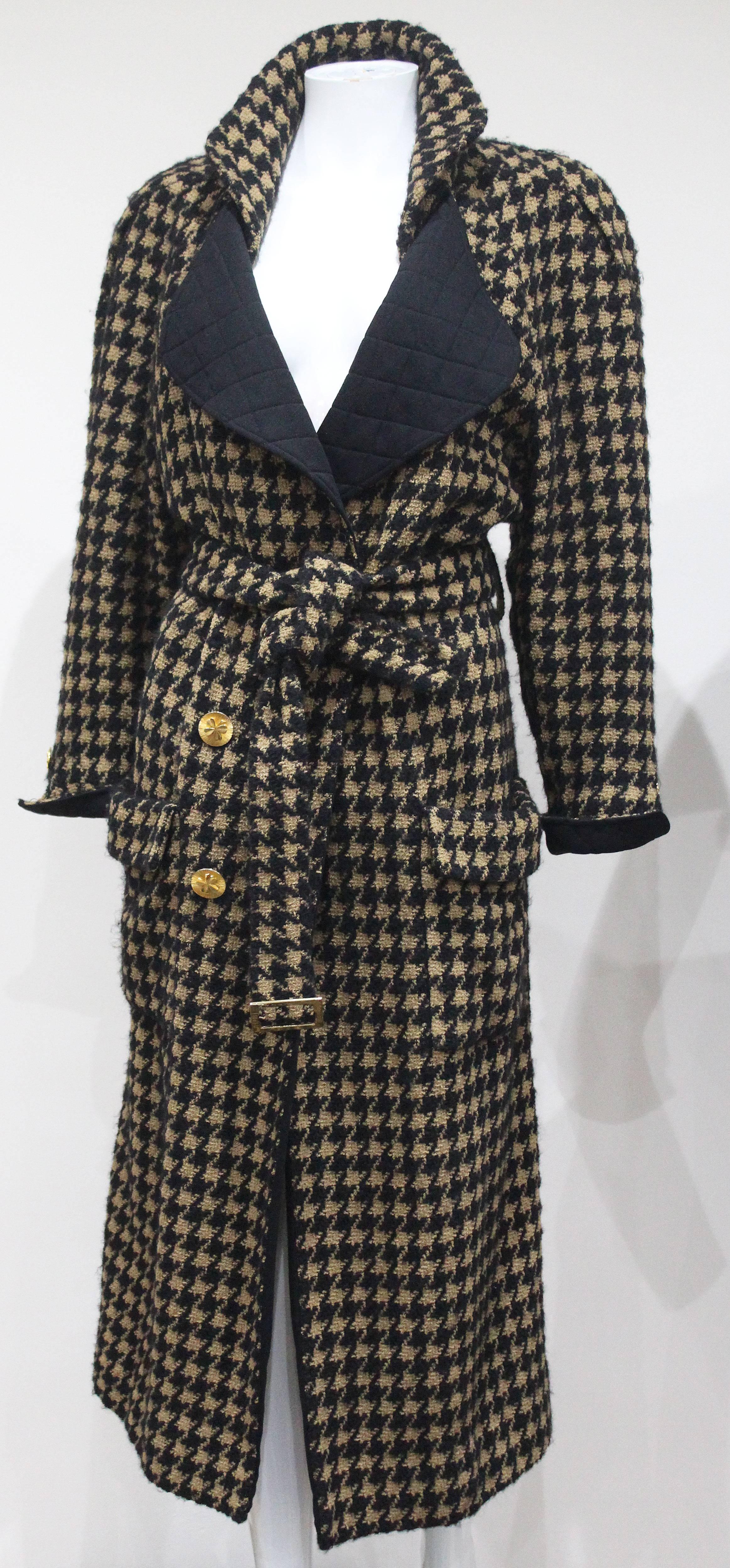 A 1980s Chanel tweed coat in a houndstooth print with quilted black collar and cuffs, gold tone Chanel buttons and matching fabric belt with gold tone Chanel stamped buckle. 

Size: Approx. Fr 38 - 40 